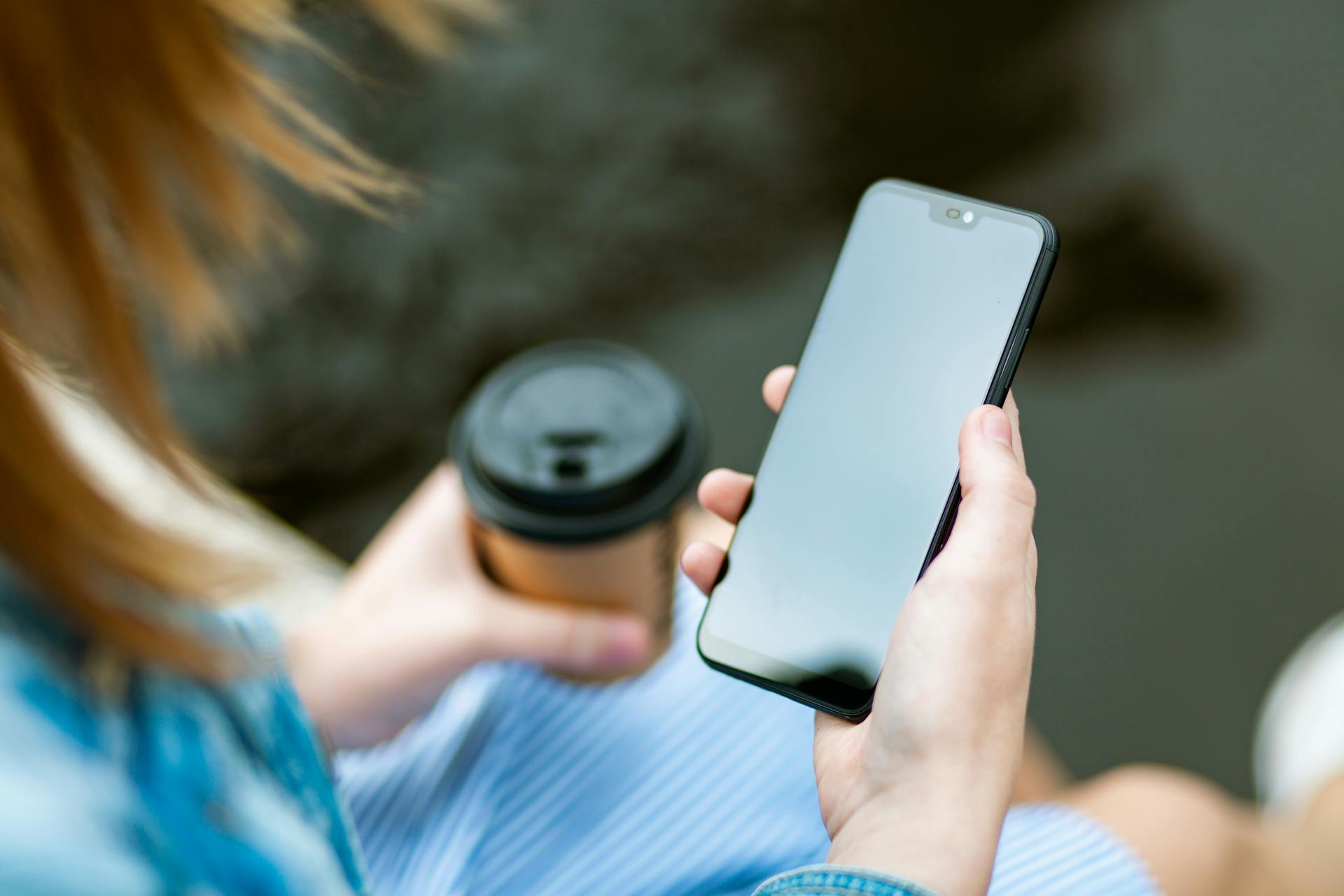 Una mujer sujetando su teléfono y una taza de café | Fuente: Pexels
