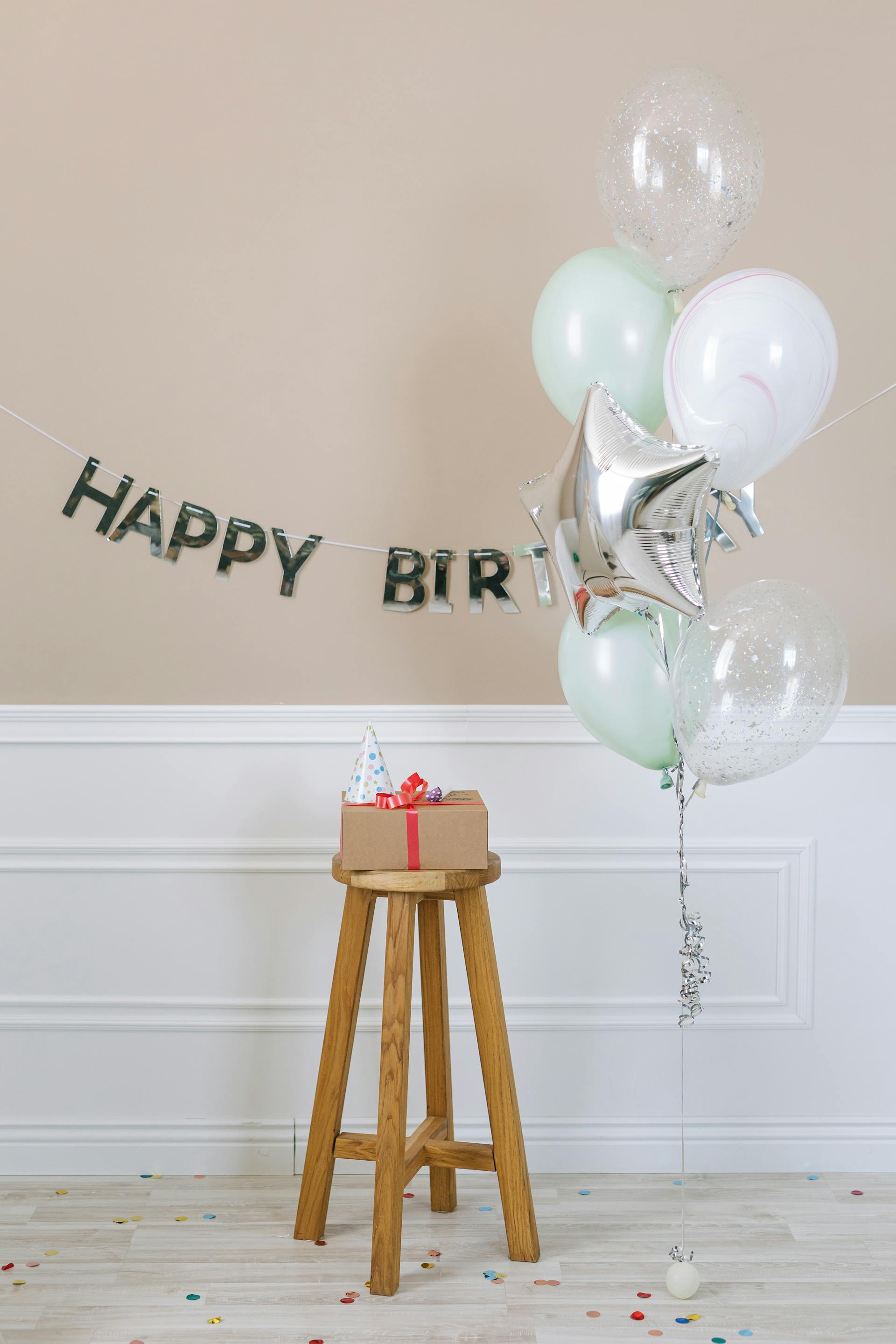Un regalo de cumpleaños sobre un taburete de madera colocado junto a globos | Fuente: Pexels