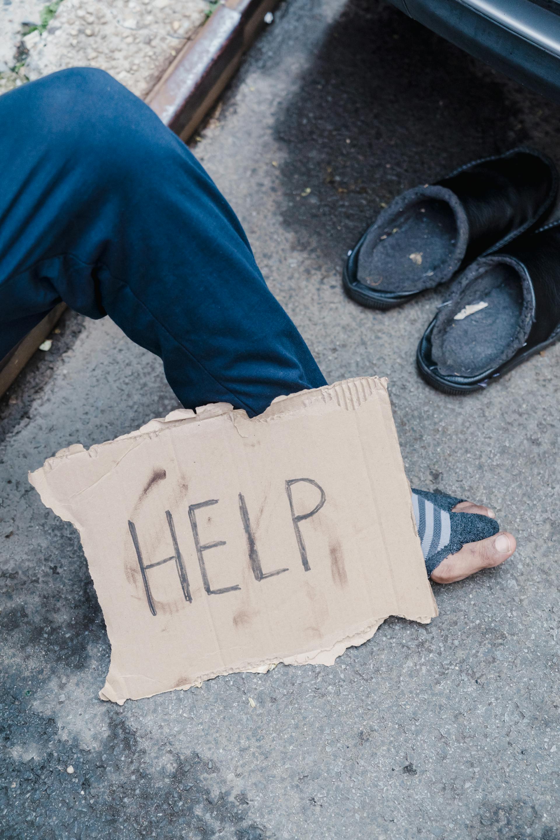 Un cartel de cartón junto a un vagabundo | Fuente: Pexels