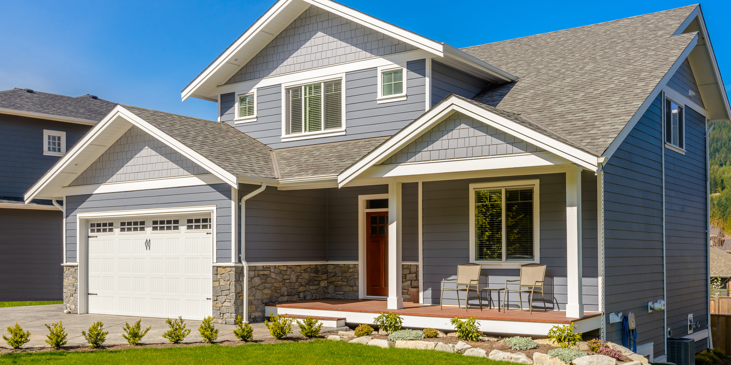 Una moderna casa gris de dos plantas de estilo Craftsman, con un porche delantero cubierto y un cuidado jardín | Fuente: Shutterstock