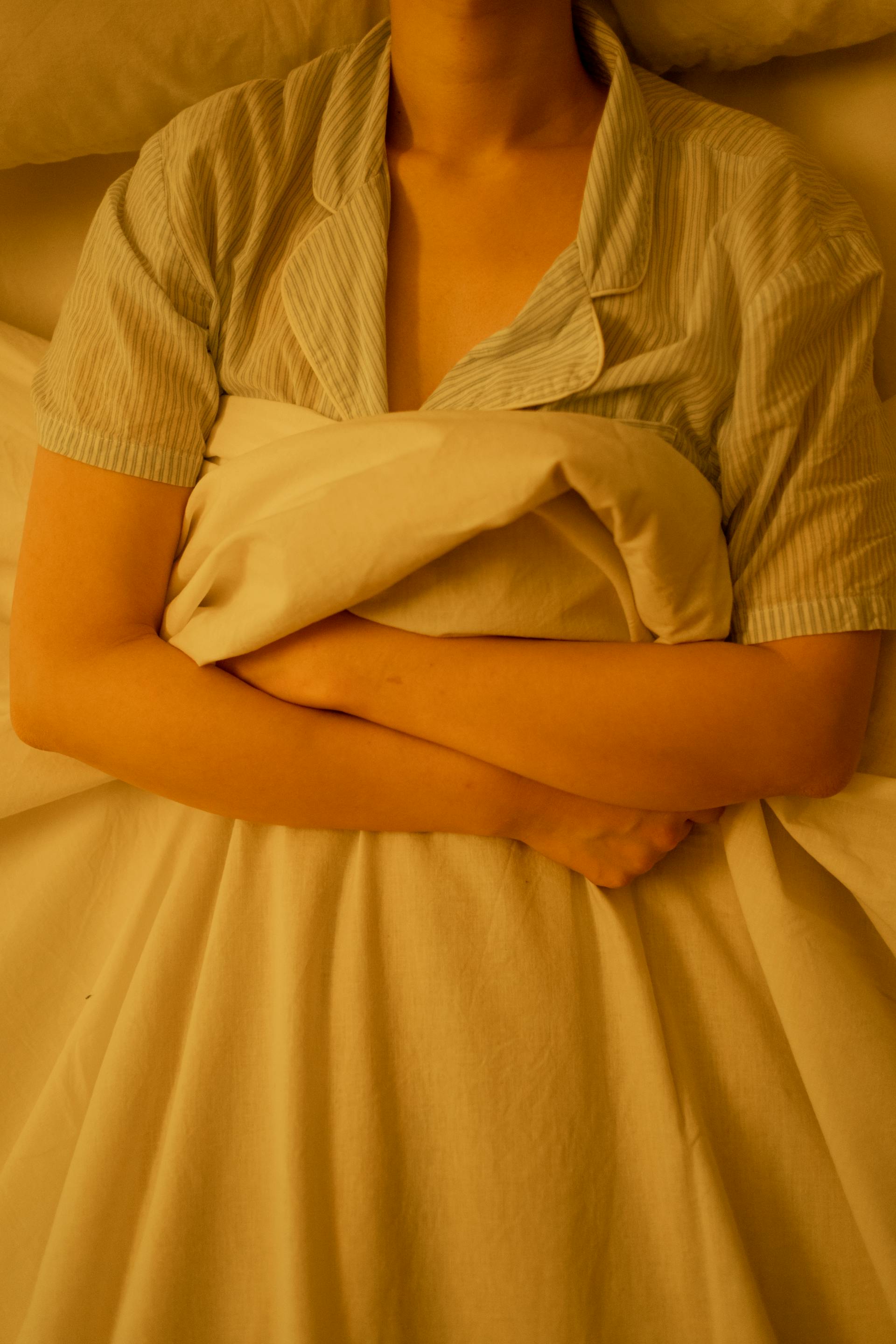 Una mujer tumbada en la cama agarrando una manta | Fuente: Pexels