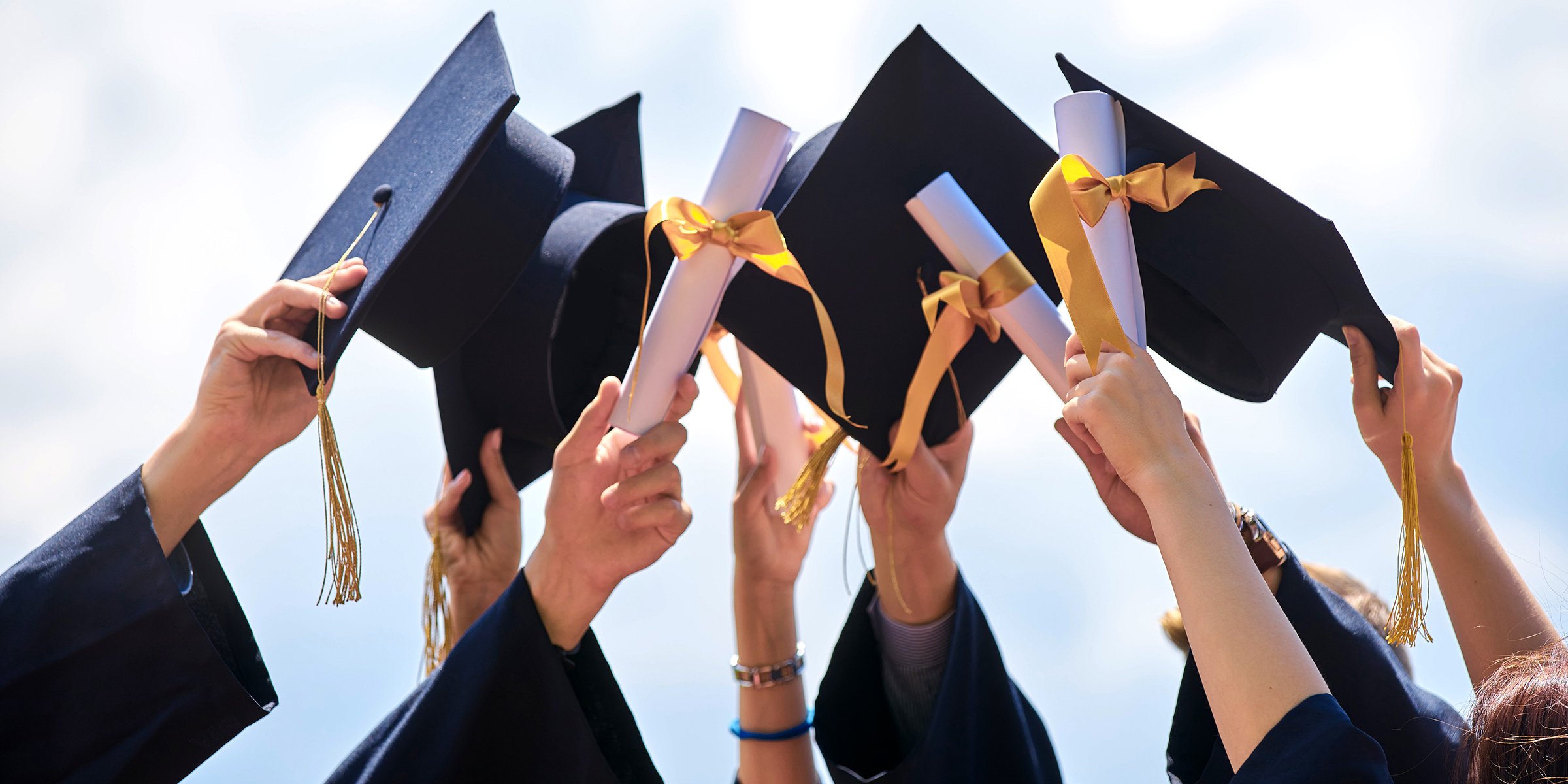 Estudiantes sujetando sus birretes de graduación | Fuente: Shutterstock