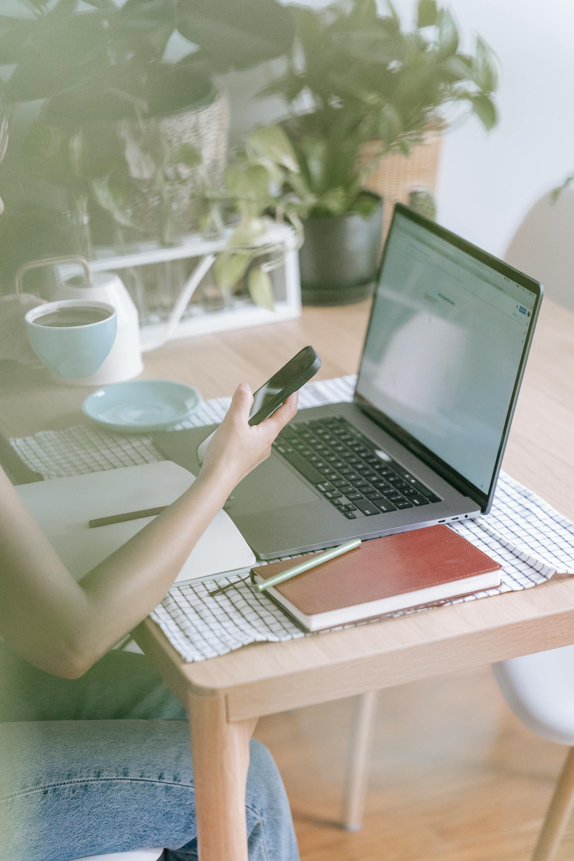 Primer plano de una mujer sujetando su teléfono mientras trabaja en su portátil | Fuente: Pexels