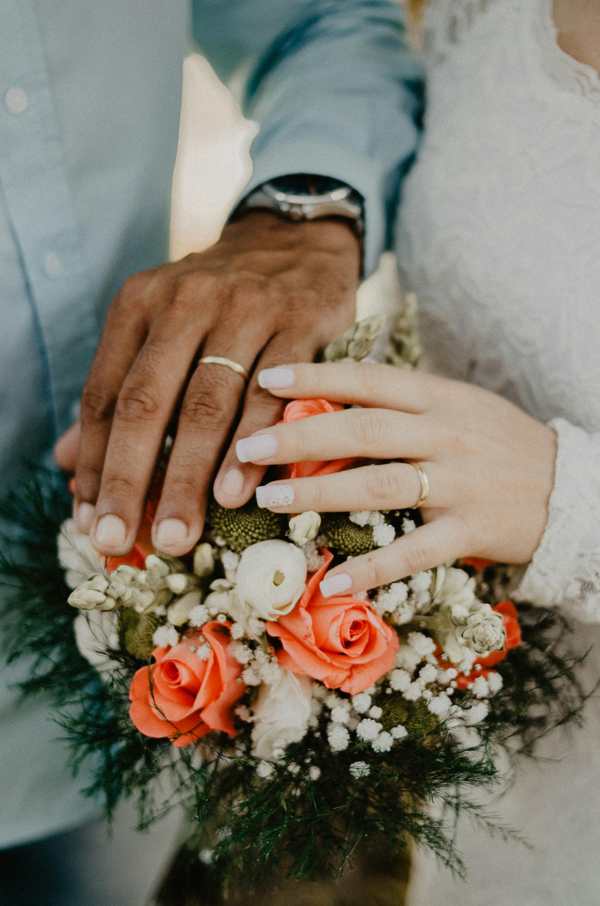 Primer plano de las manos de unos novios sobre un ramo | Fuente: Pexels