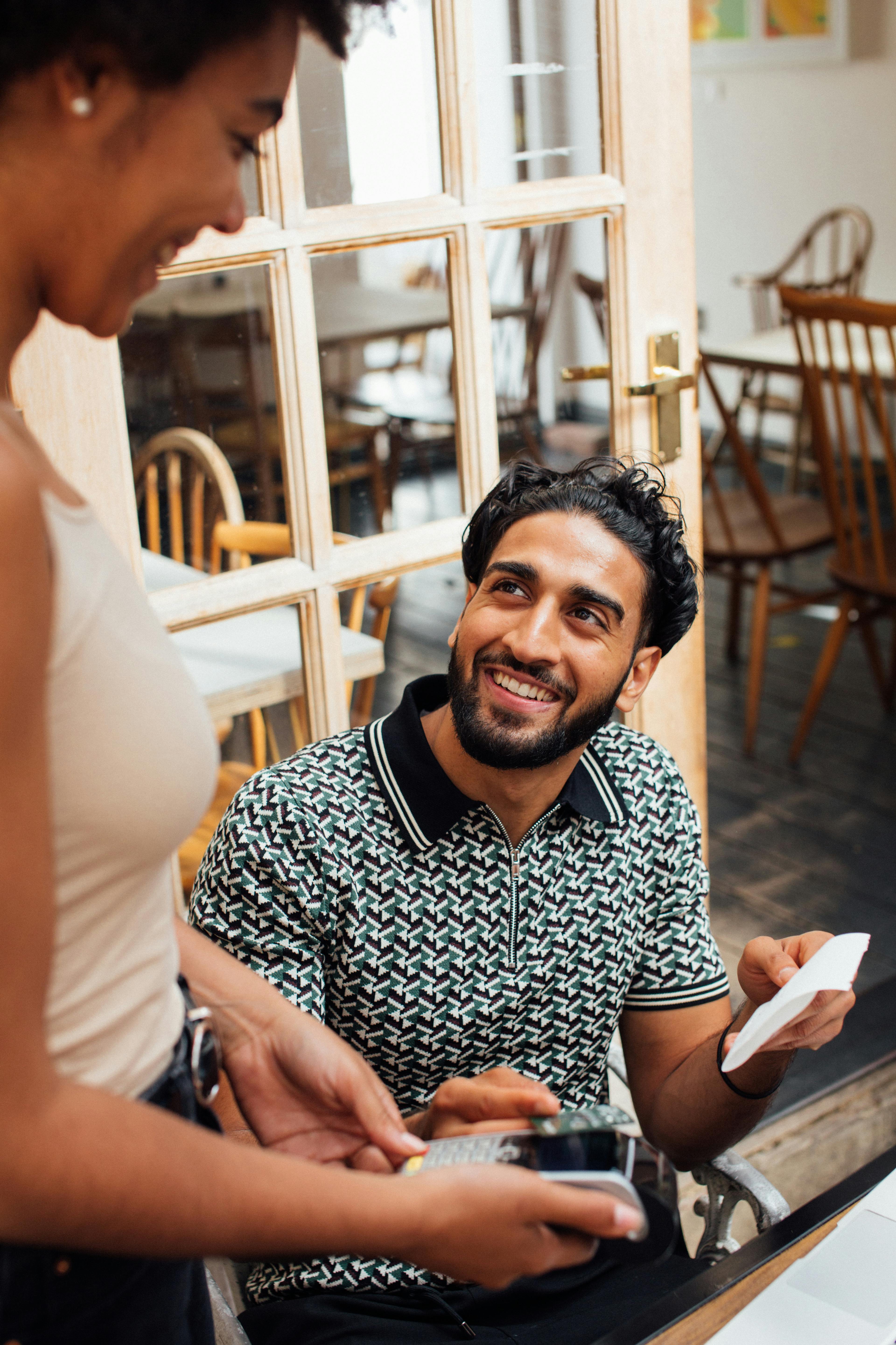 Hombre sonriendo mientras habla con una camarera | Fuente: Pexels