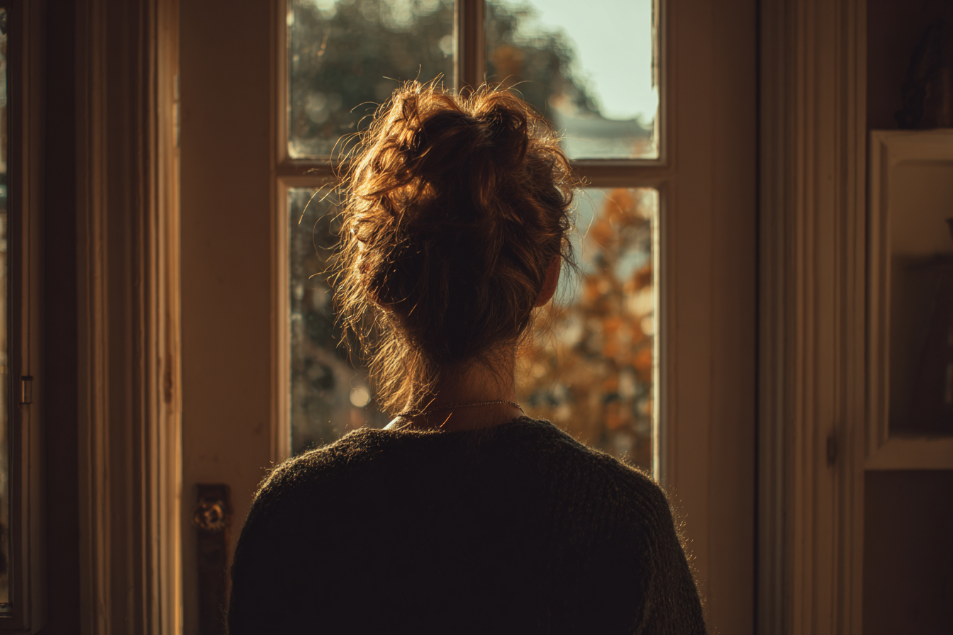 Una mujer mirando por la ventana | Fuente: Midjourney
