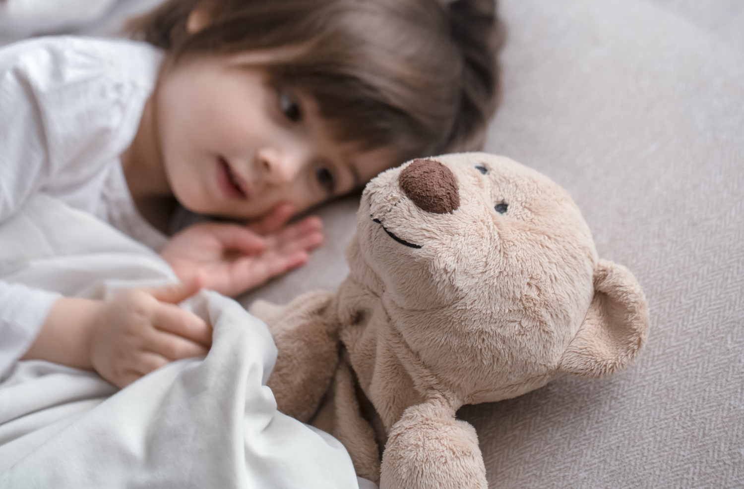 Una niña tumbada junto a su osito de peluche | Fuente: Freepik