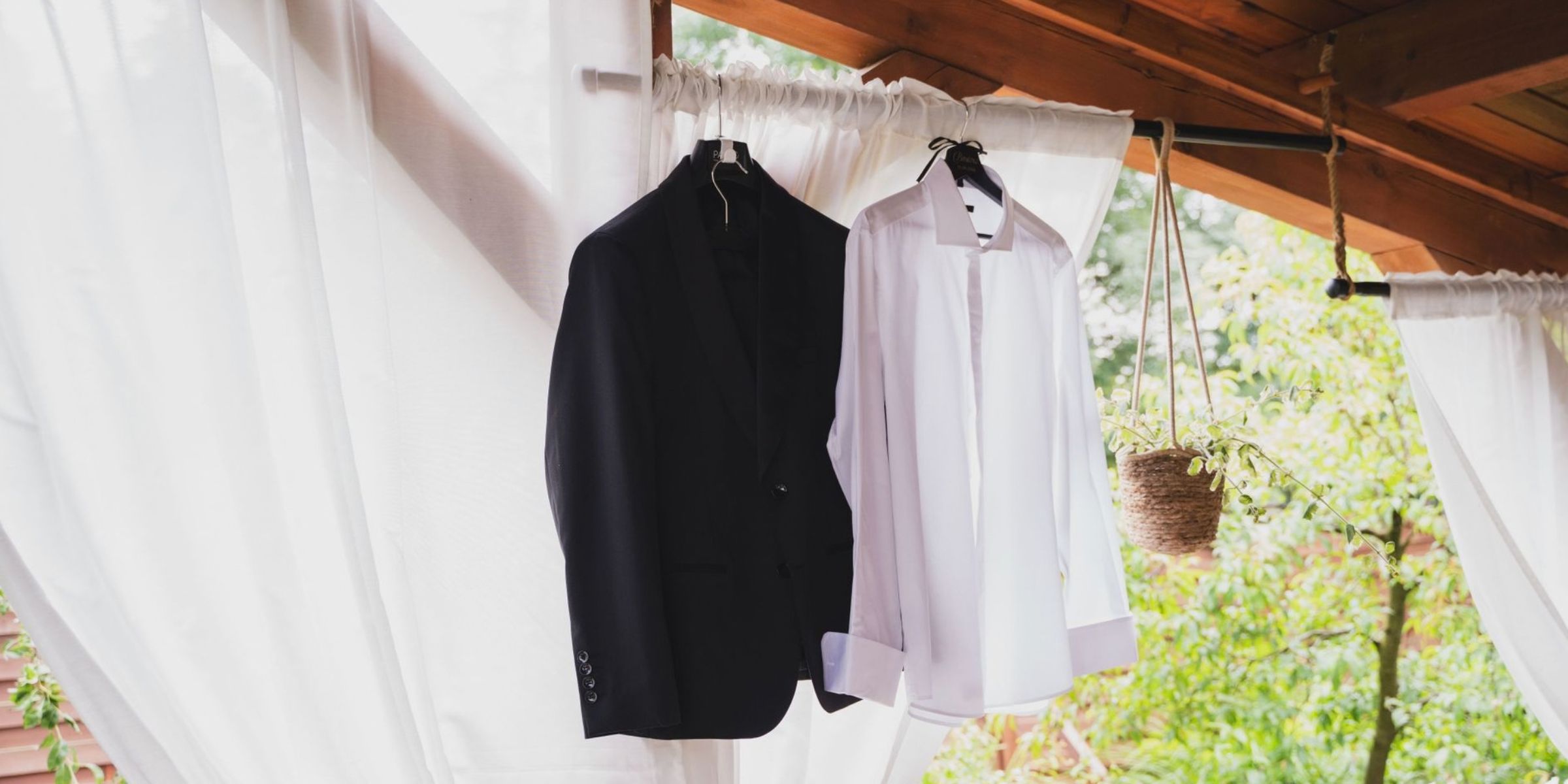 A black suit and a white shirt hang on a wooden frame outdoors | Source: Pexels
