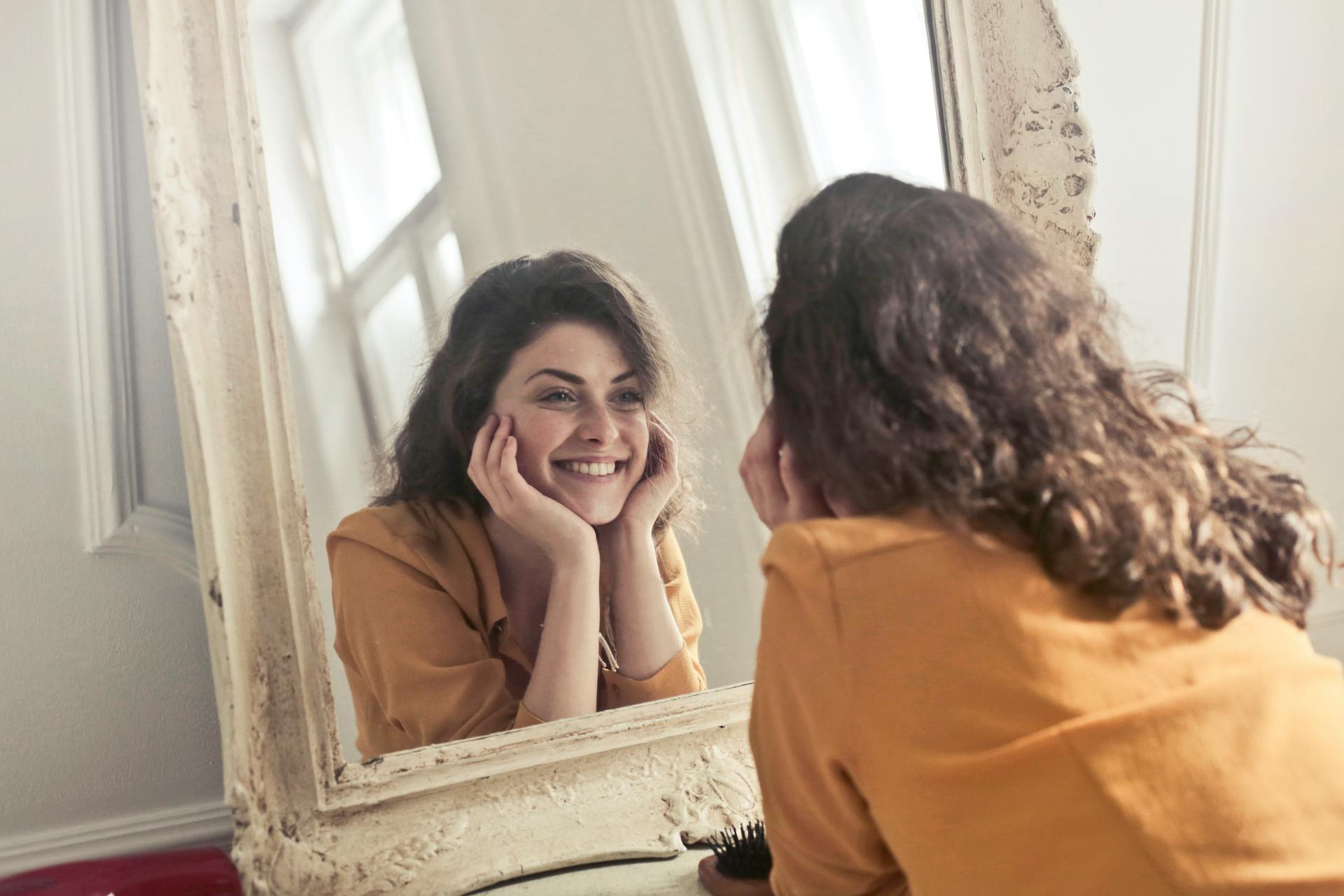 Uma mulher sorridente olhando seu reflexo no espelho | Fonte: Pexels