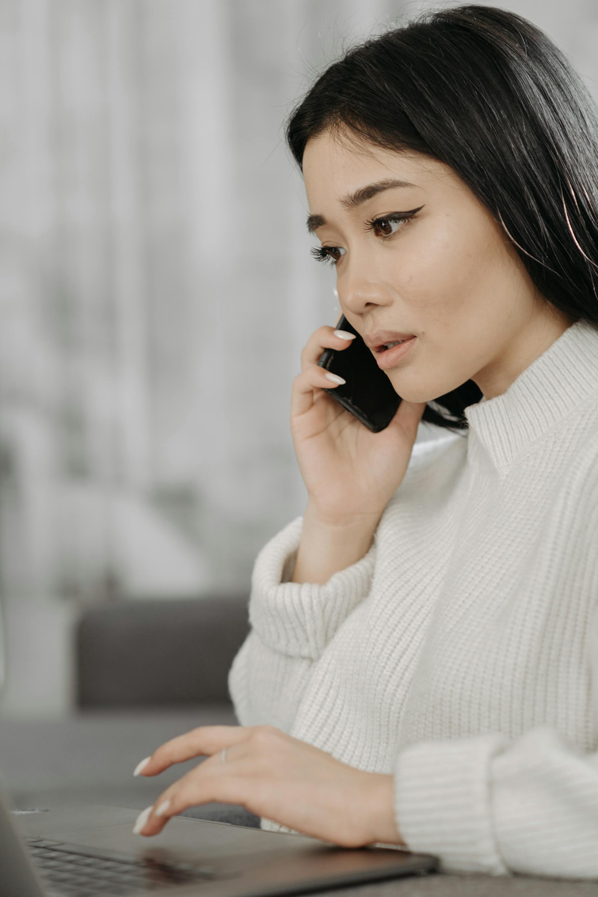 Una mujer con expresión triste hablando por teléfono mientras trabaja | Fuente: Pexels