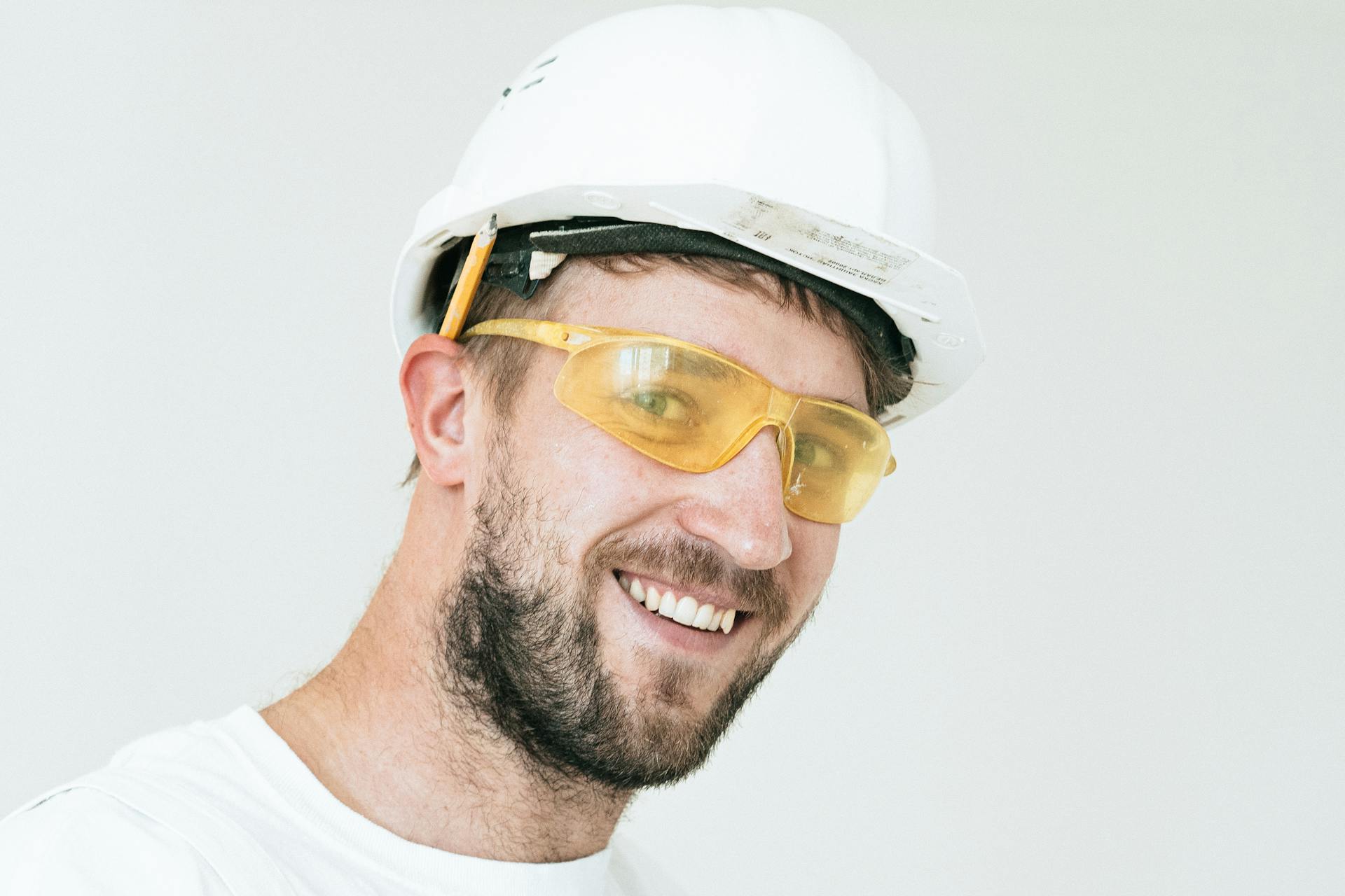 Un obrero de la construcción sonriente con casco blanco y gafas de seguridad amarillas | Fuente: Pexels