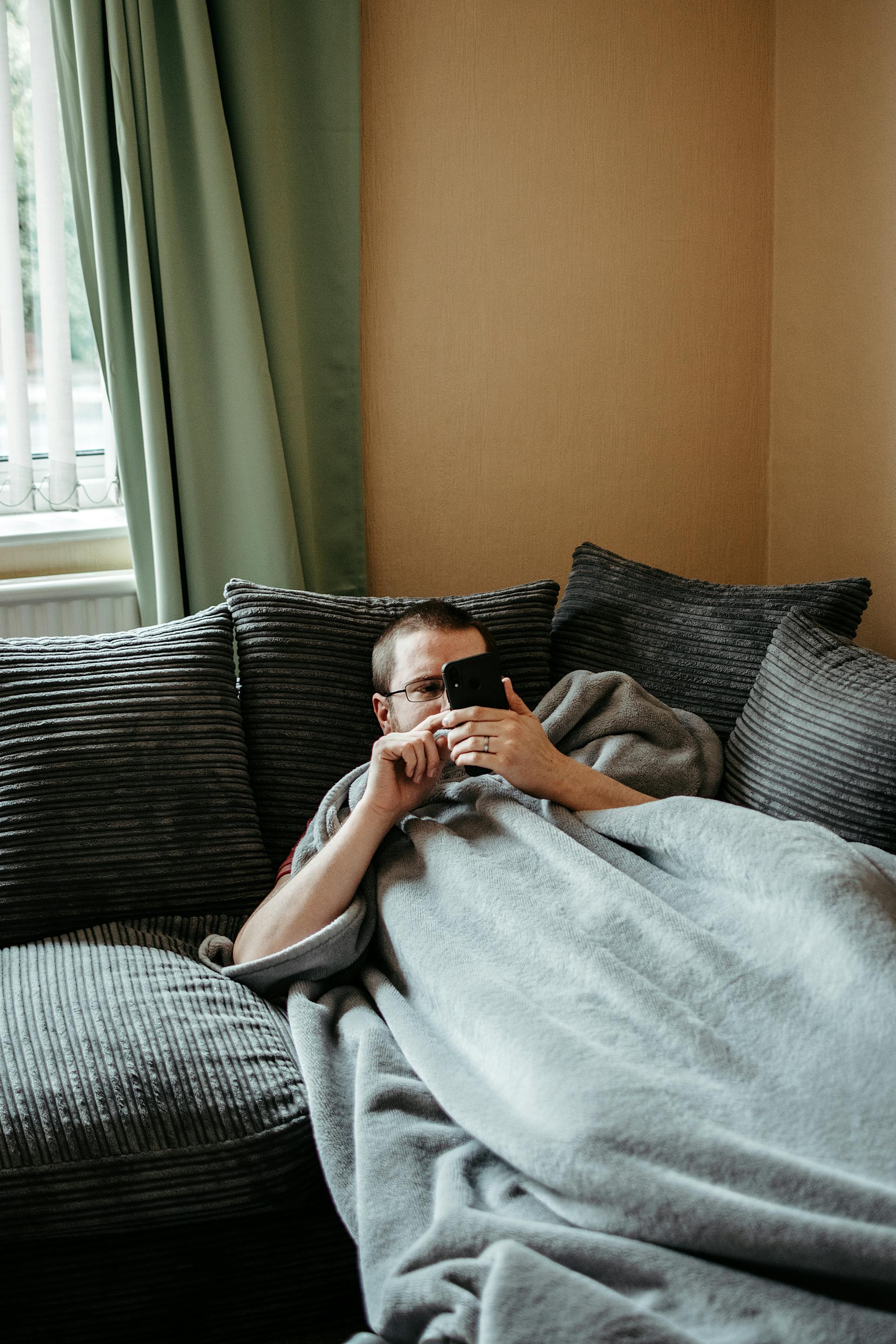 Un hombre usando su teléfono mientras está tumbado en el sofá | Fuente: Pexels