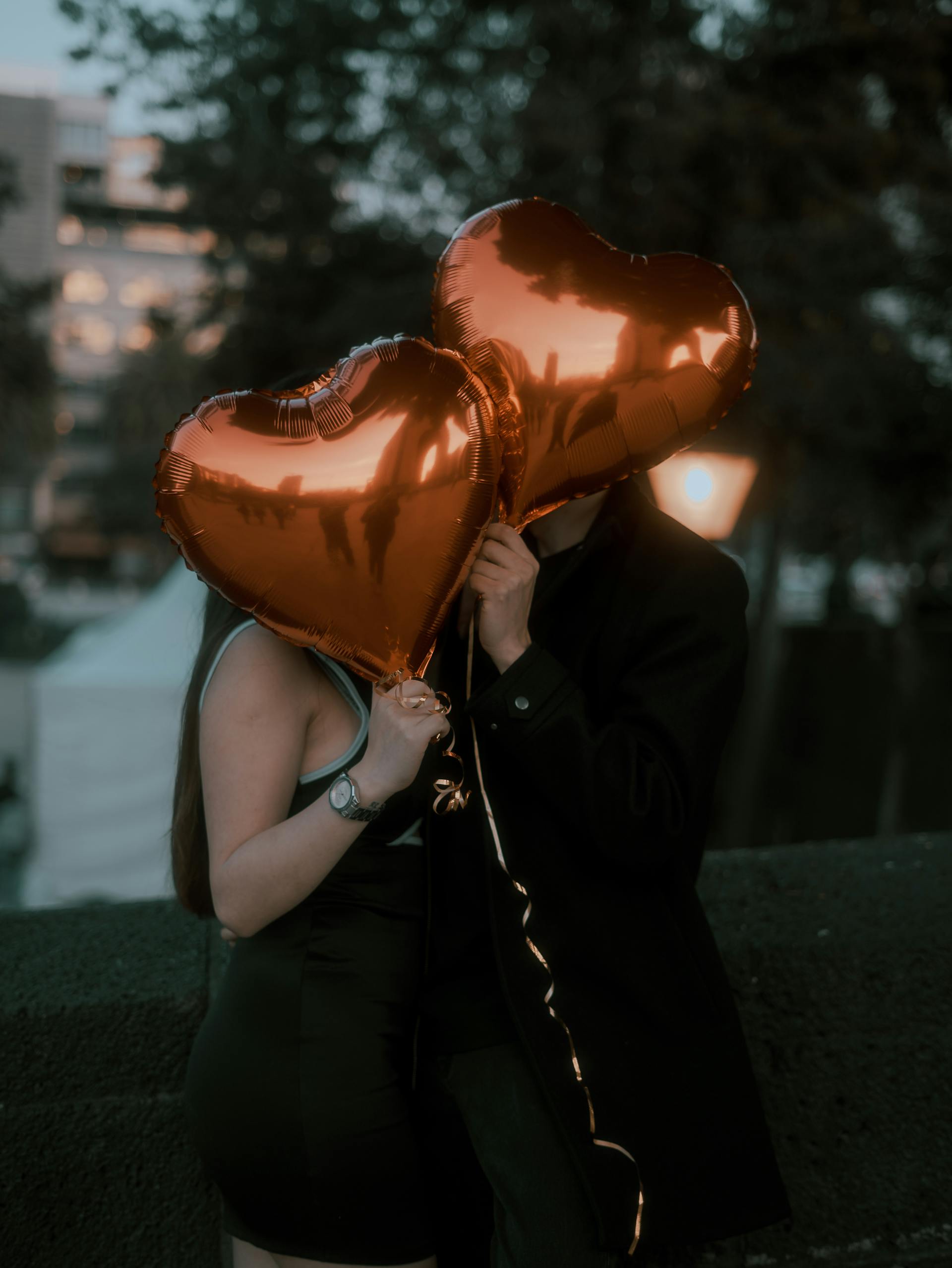 Una pareja ocultando sus rostros con globos en forma de corazón | Fuente: Pexels