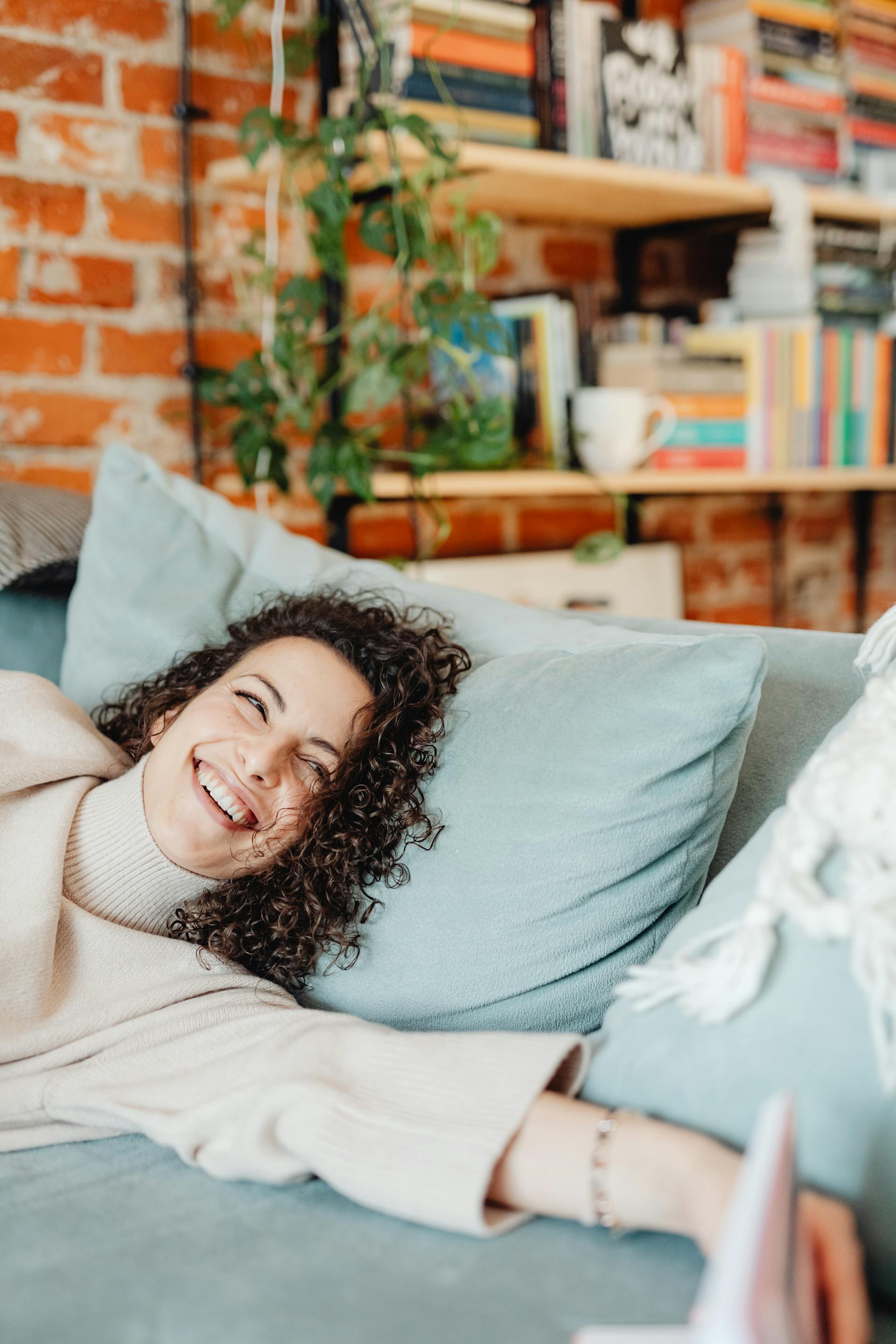 Una mujer feliz tumbada en un sofá con una sonrisa en la cara | Fuente: Pexels