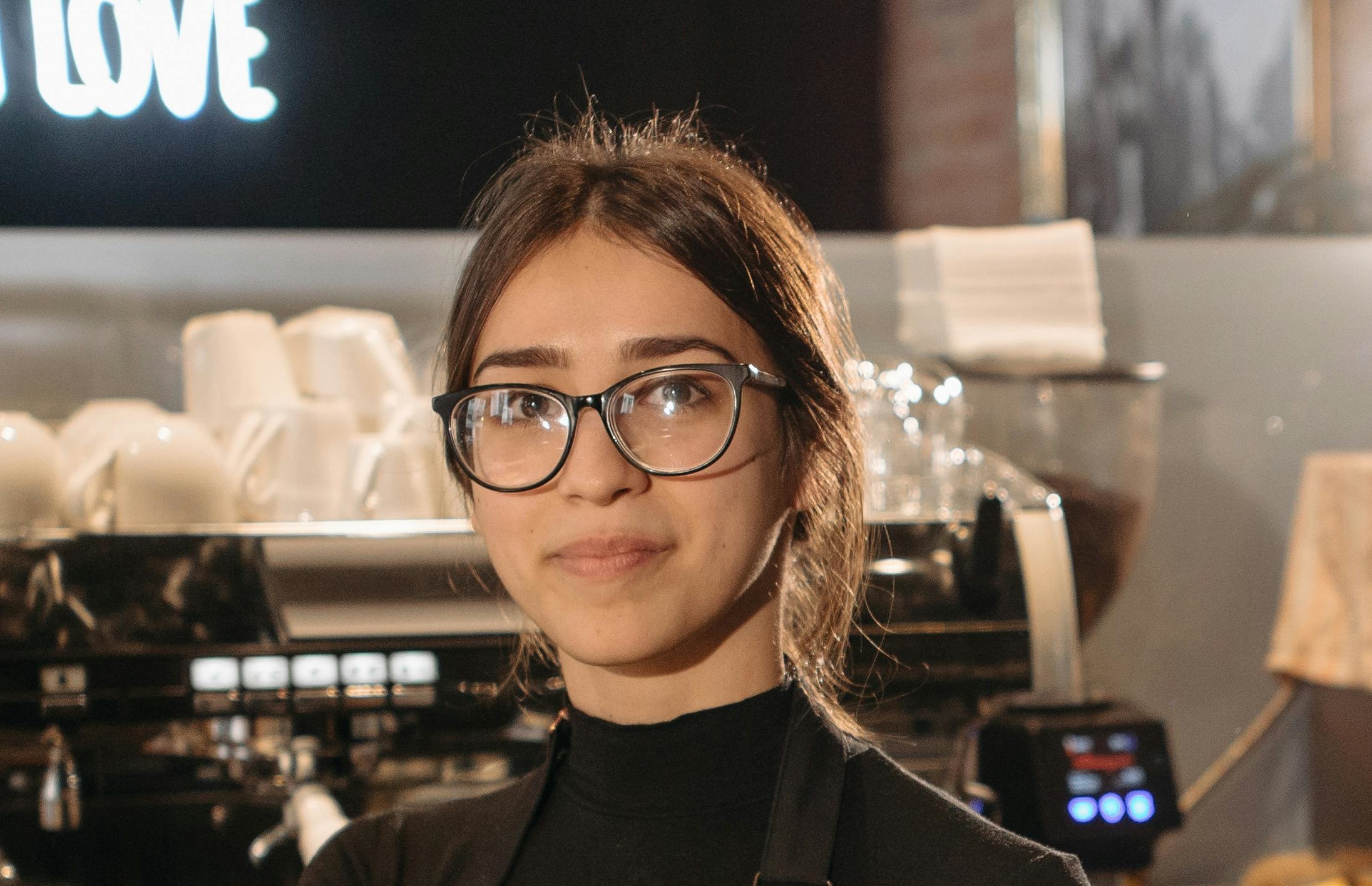 Una camarera feliz con gafas mirando a lo lejos mientras está de pie en una cafetería | Fuente: Pexels