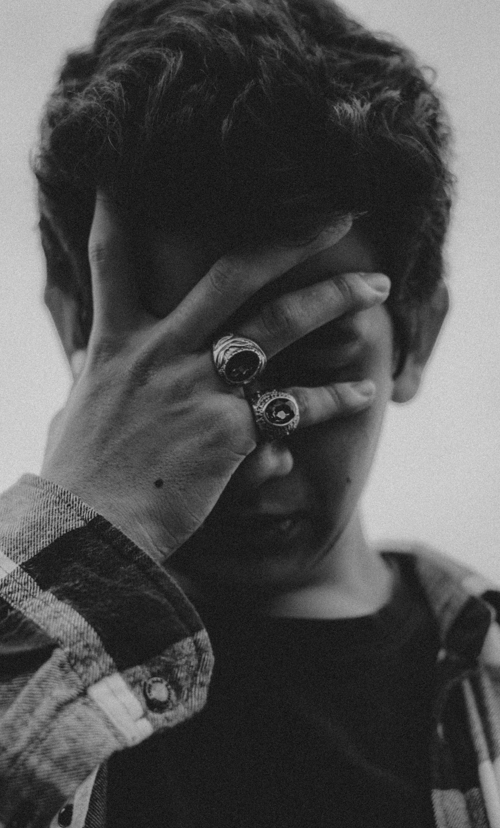 Foto en escala de grises de un joven tapándose la cara | Fuente: Pexels