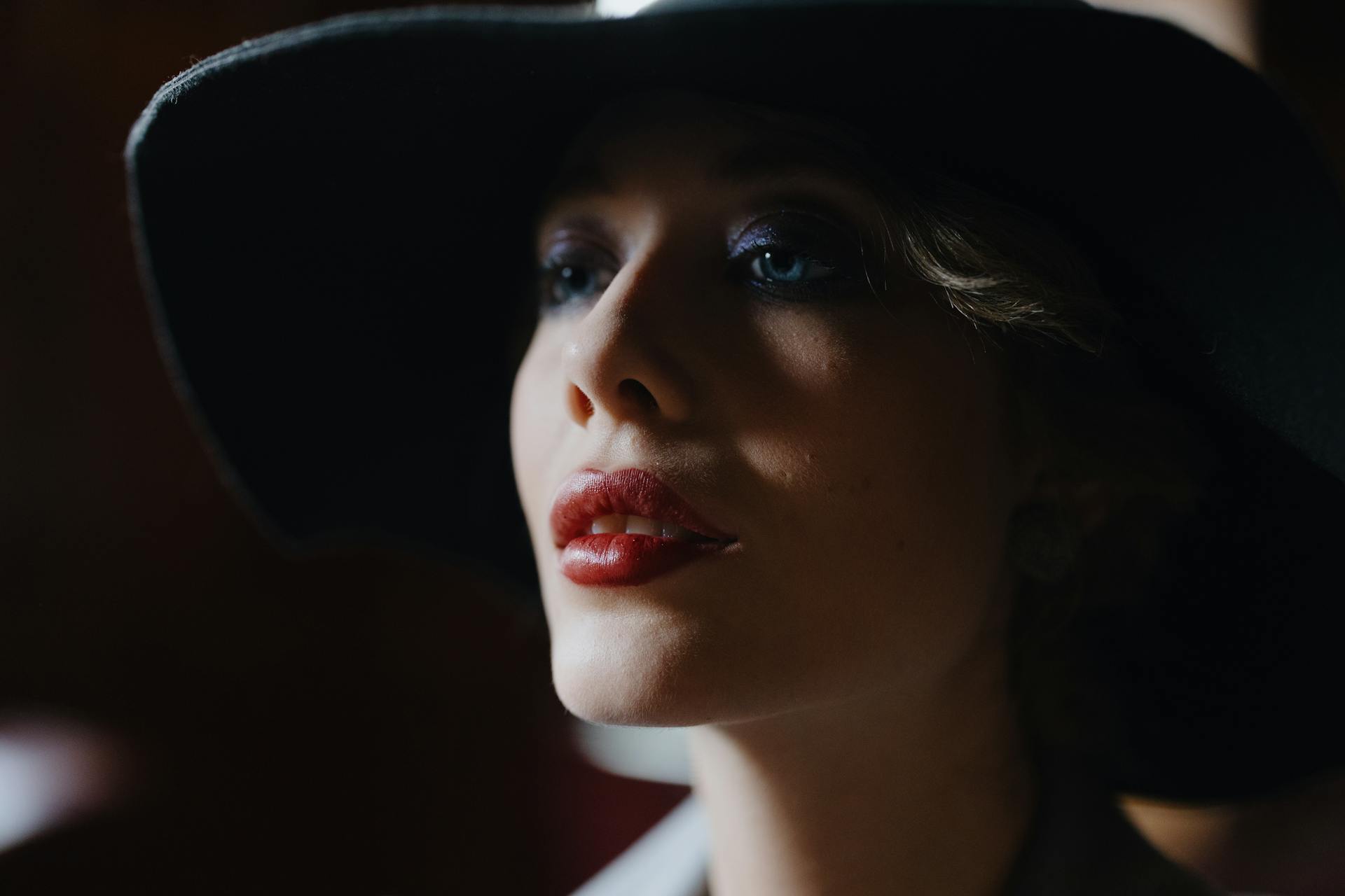 Una bella mujer con los labios pintados de rojo y un sombrero negro mirando a un lado | Fuente: Pexels