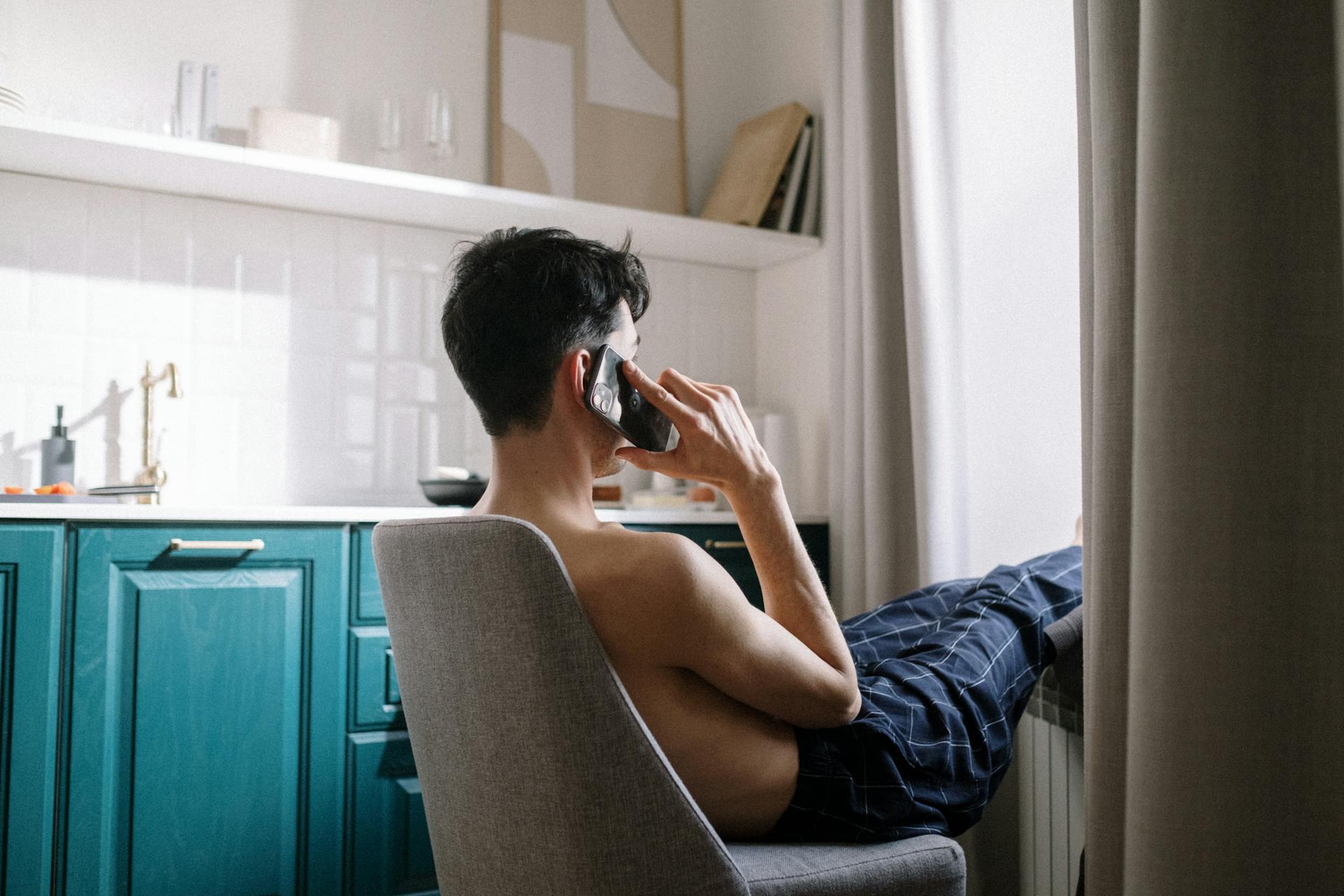 Vista lateral de un hombre sentado en una silla y hablando por teléfono | Fuente: Pexels
