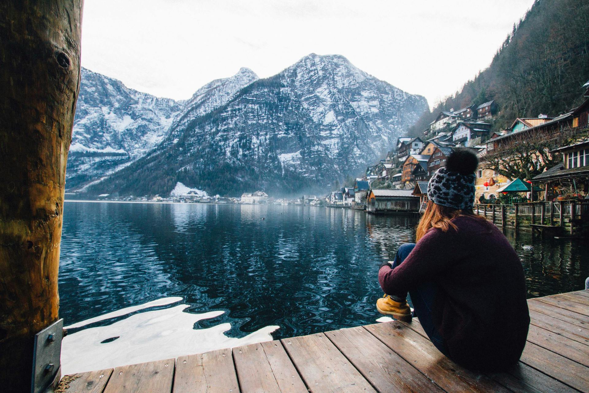 Una mujer sentada en una terraza de madera, contemplando el lago y las montañas | Fuente: Pexels