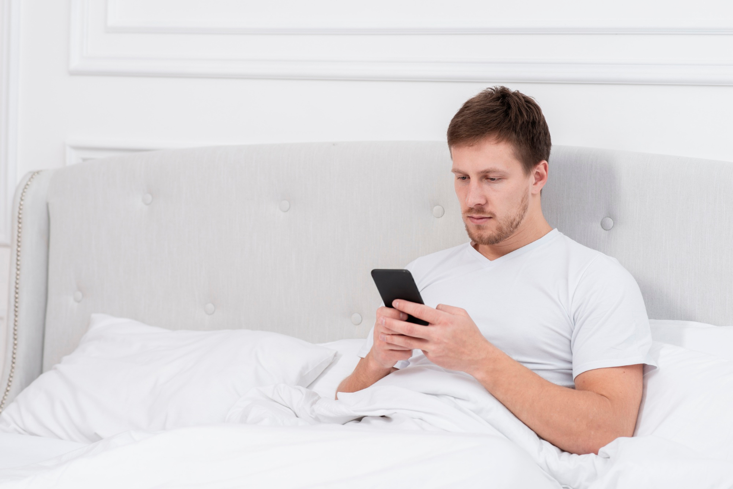 Un hombre sentado en su cama y mirando su teléfono | Fuente: Freepik