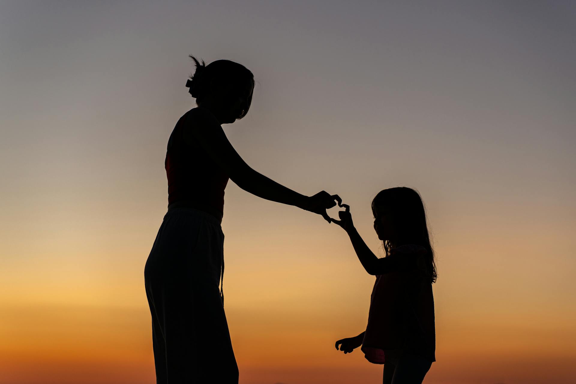 Silueta de una madre y su hija haciendo un gesto de corazón con la mano | Fuente: Pexels