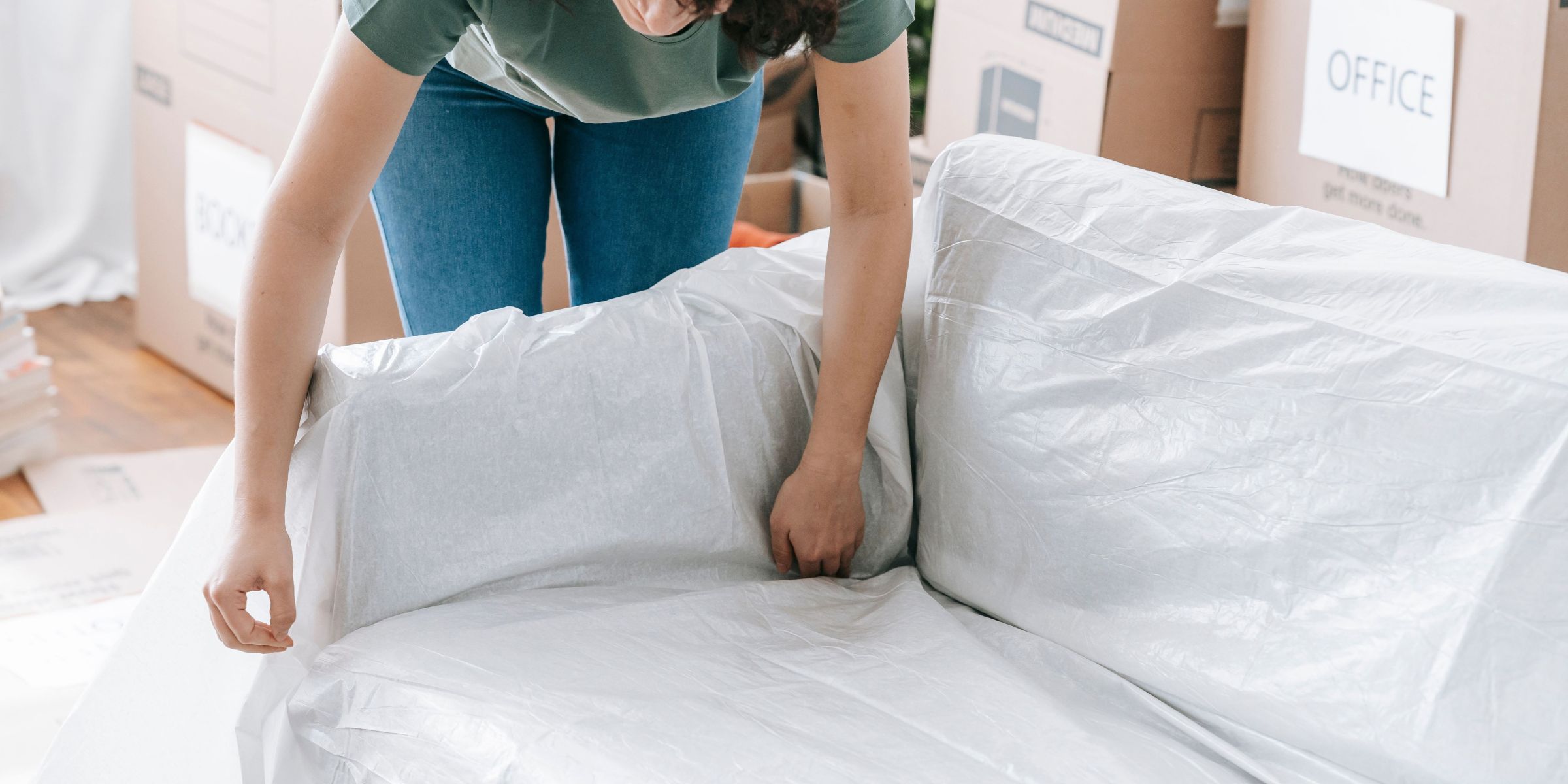 A woman carefully wraps a sofa in protective material | Source: Pexels