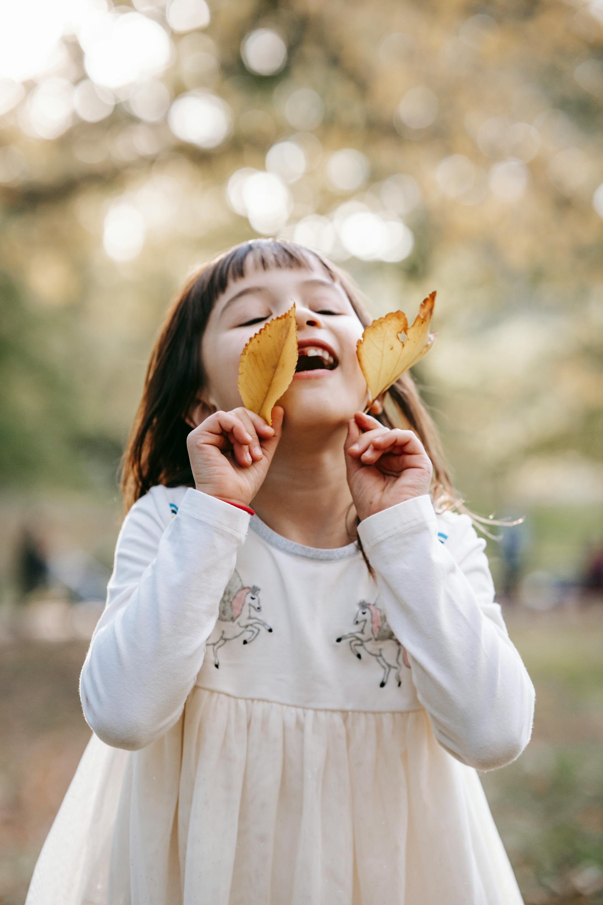 Una niña feliz con hojas amarillas de pie en un parque | Fuente: Pexels