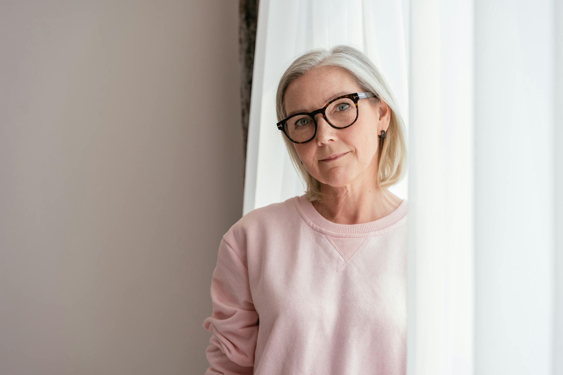 Mujer de mediana edad con jersey rosa y gafas | Fuente: Pexels