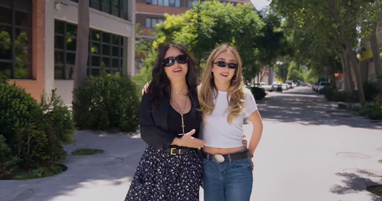 Salma y Valentina iban cogidas del brazo antes de seguir con su ruta de compras vintage. Sus conjuntos, tan diferentes, reflejaban las diferencias de estilo de las que habían hablado: Salma había elegido una falda oscura con estampado floral y Valentina llevaba una camiseta corta blanca con vaqueros holgados. | Fuente: YouTube/Instagram