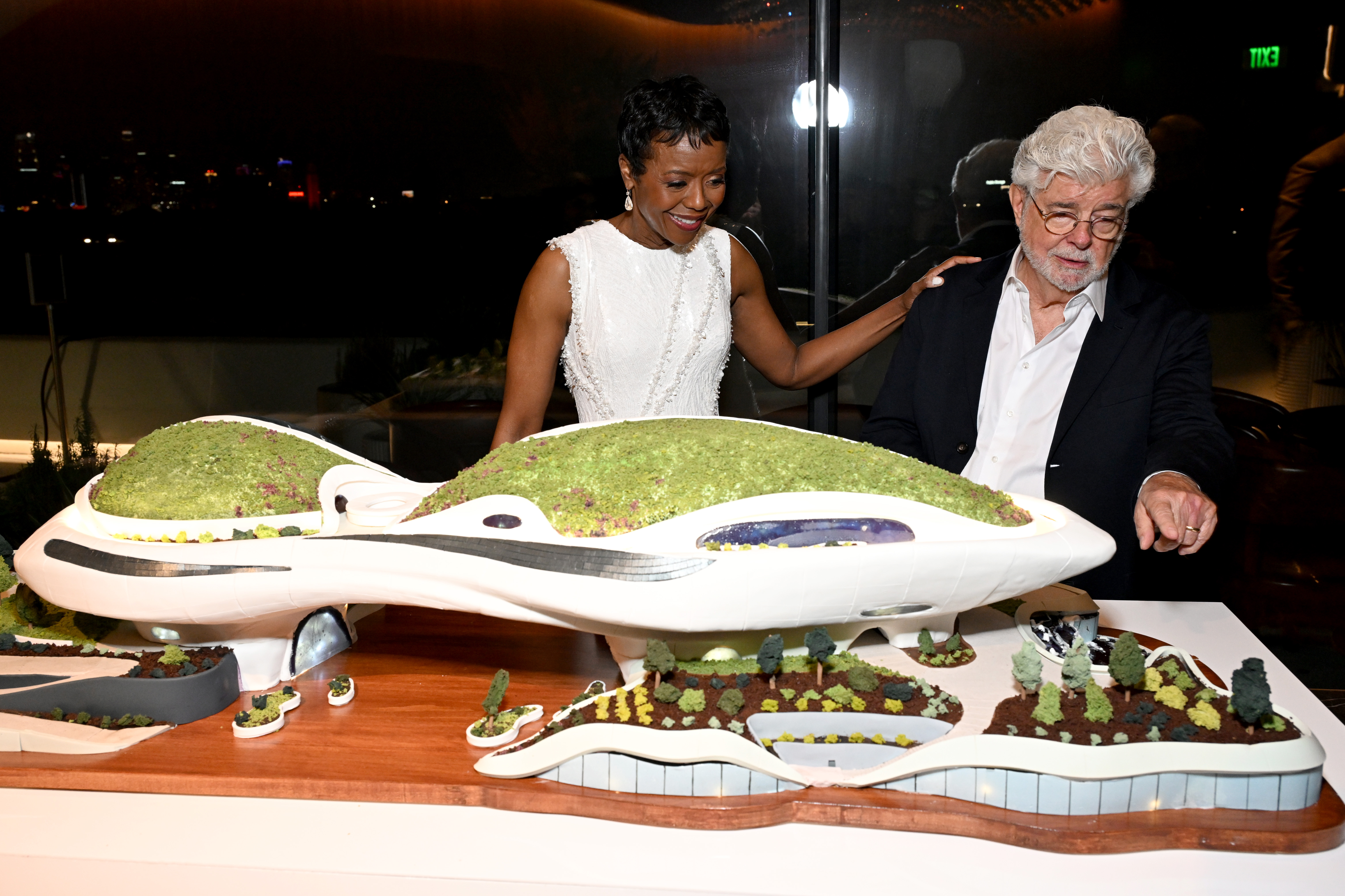 George Lucas y Mellody Hobson posaron juntos junto a una maqueta detallada del Museo Lucas y sus jardines. Hobson apoyó una mano en el hombro de Lucas mientras los cofundadores contemplaban la exposición. | Fuente: Getty Images