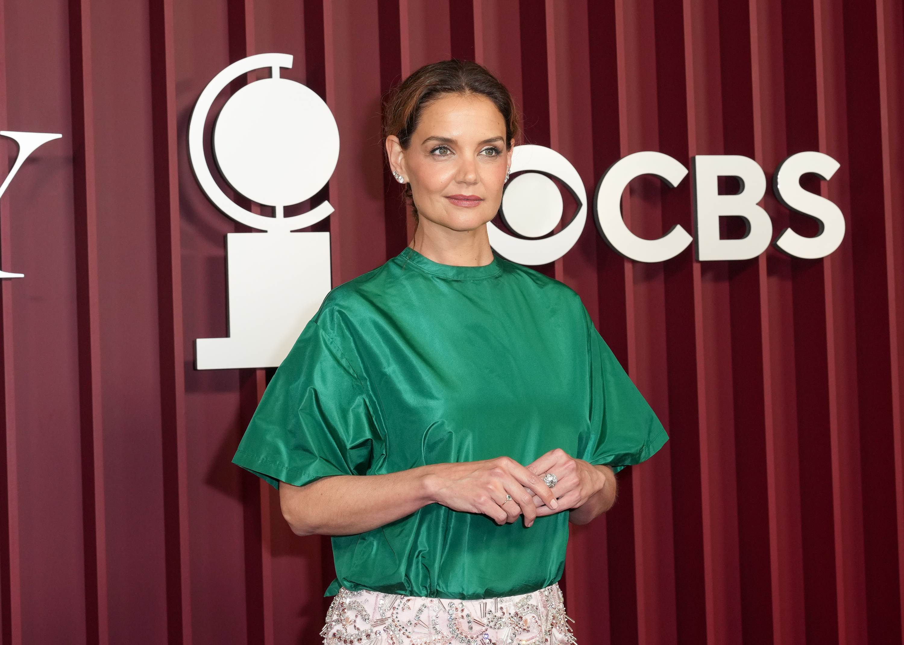 Vestida con una atrevida combinación de colores, Katie Holmes aparece equilibrada con una blusa de satén verde y un maquillaje de tonos suaves, de pie frente a los logotipos de la CBS y los Tony, mientras llega para presentarse en la noche más importante de Broadway en la ciudad de Nueva York.