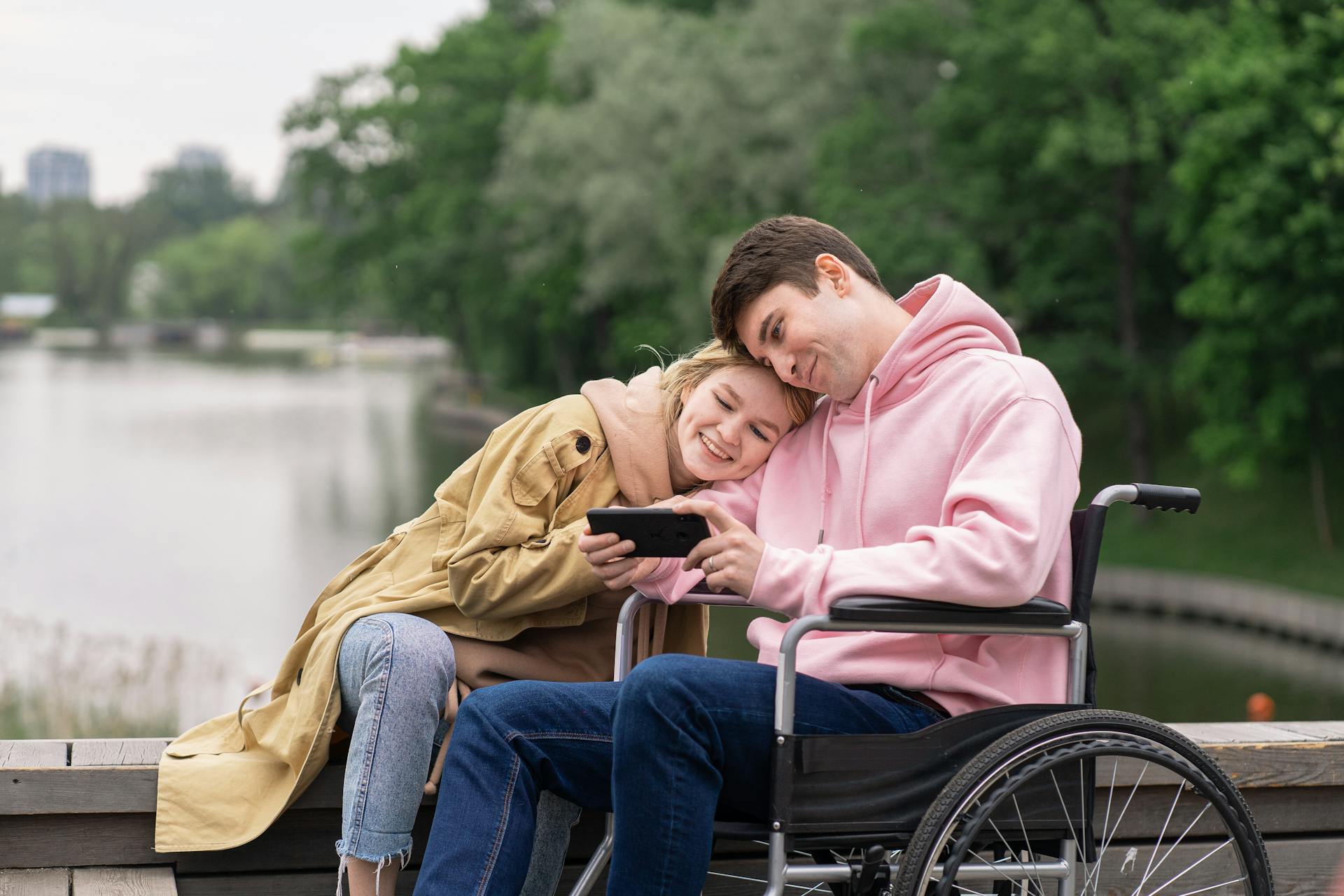 Un hombre en silla de ruedas mira un smartphone junto a su esposa | Fuente: Pexels