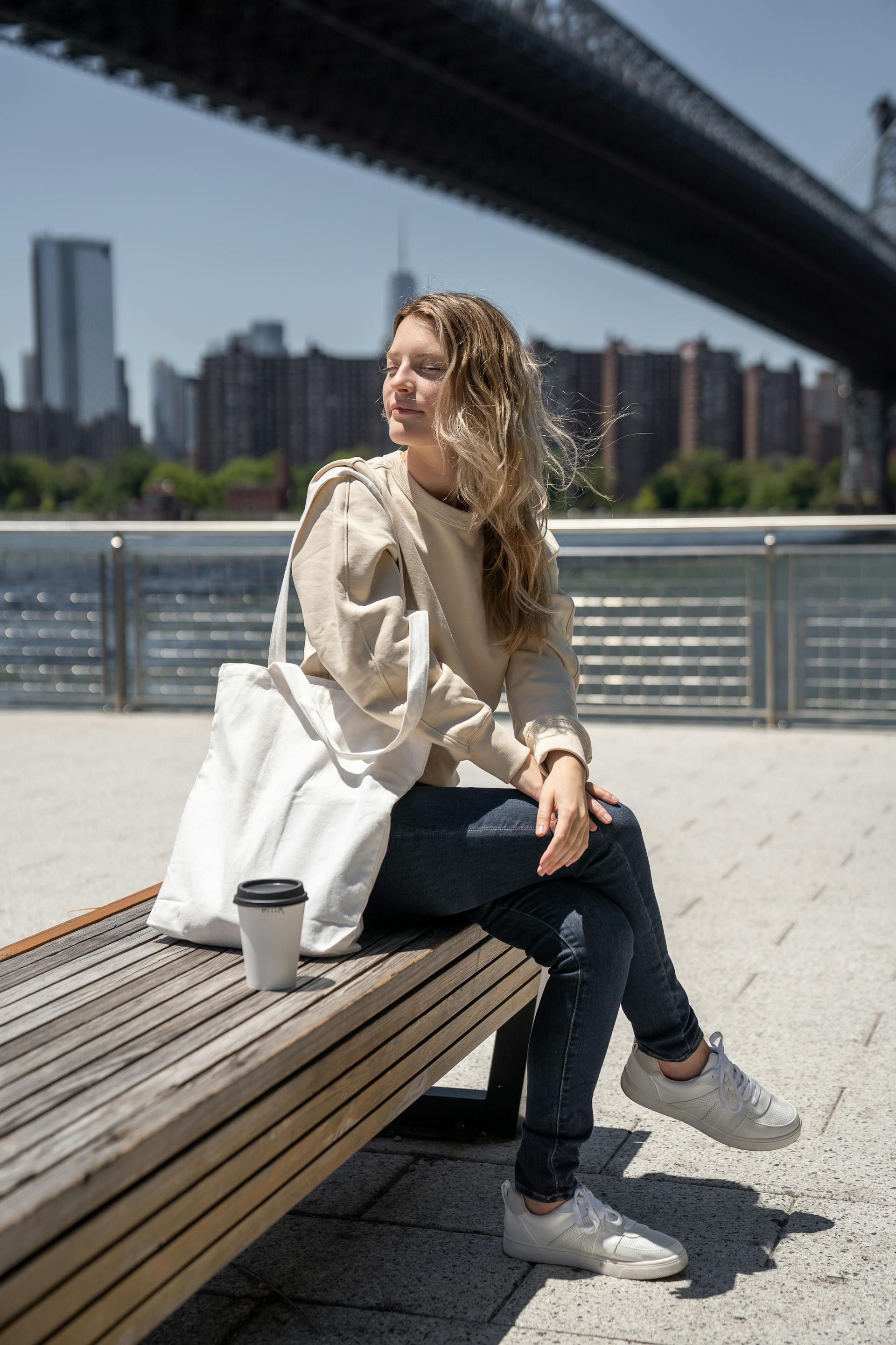Una mujer sentada en un banco con su bolso blanco y un café | Fuente: Pexels