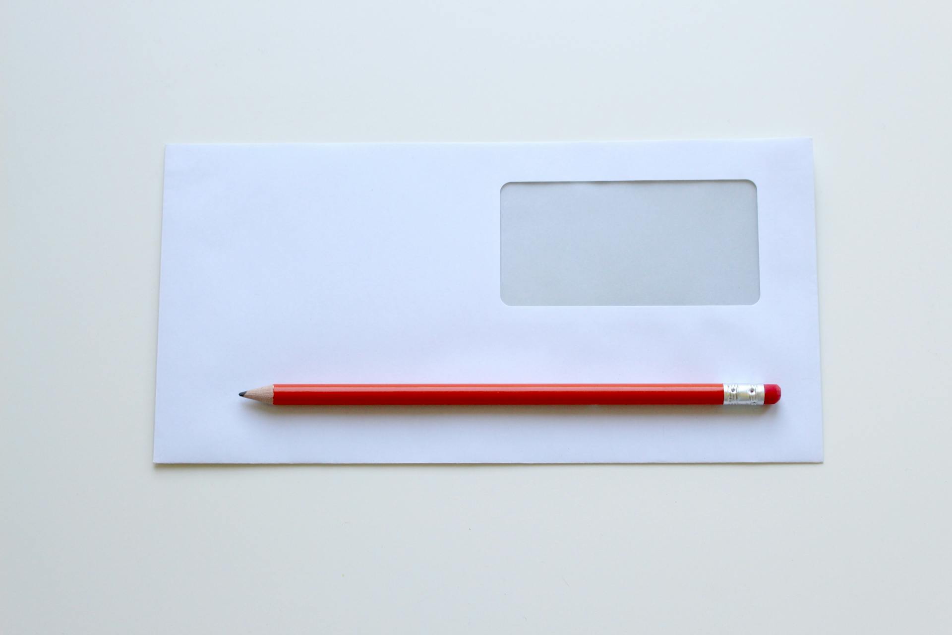 Lápiz rojo tumbado sobre un sobre blanco | Fuente: Pexels