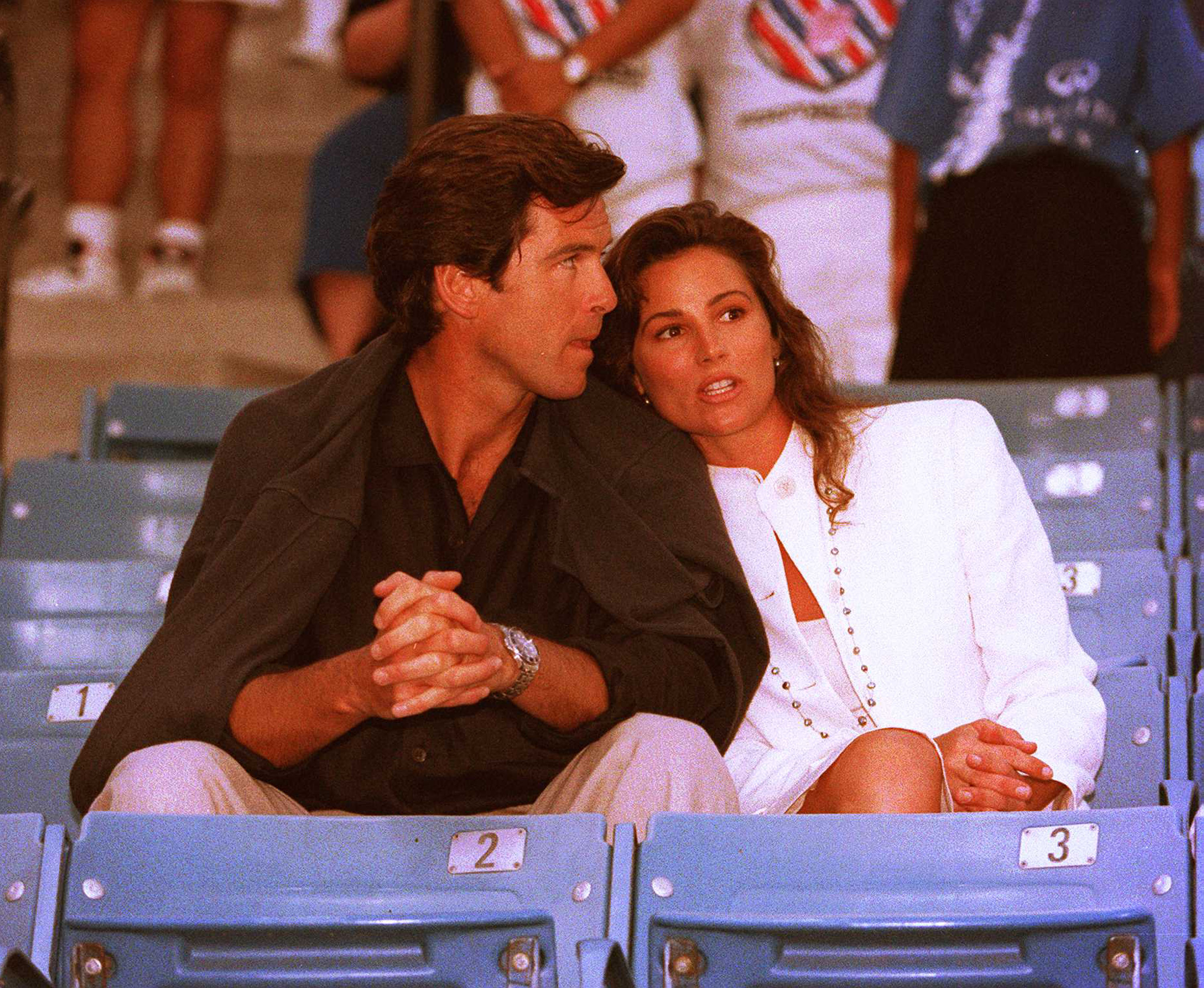 Pierce Brosnan y Keely Shaye Smith compartieron un momento de intimidad mientras veían el Torneo de Tenis Infiniti en Westwood, California, el 31 de julio de 1995. | Fuente: Getty Images.
