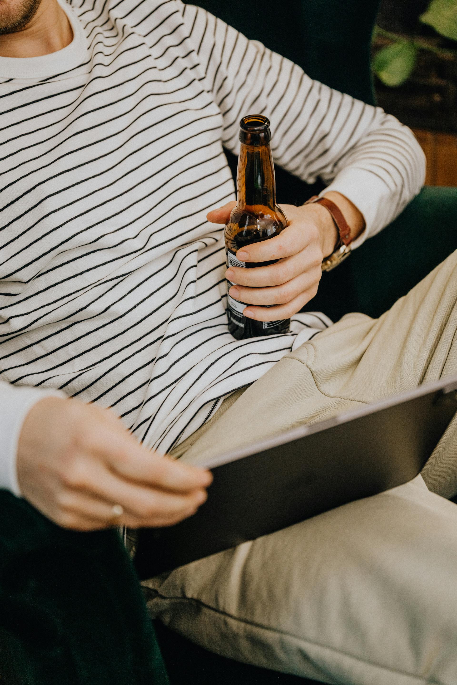 Primer plano de un hombre que sostiene una botella de cerveza y mira su tableta | Fuente: Pexels