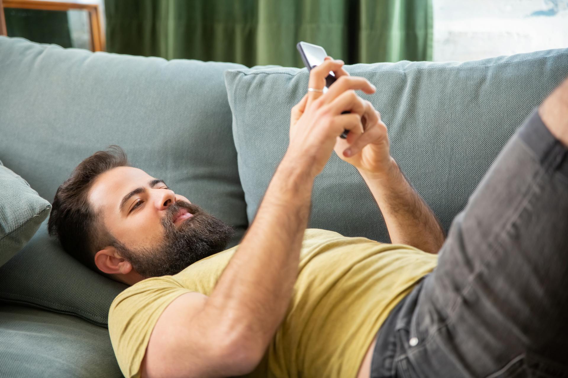 Un hombre usando su teléfono tumbado en el sofá | Fuente: Pexels