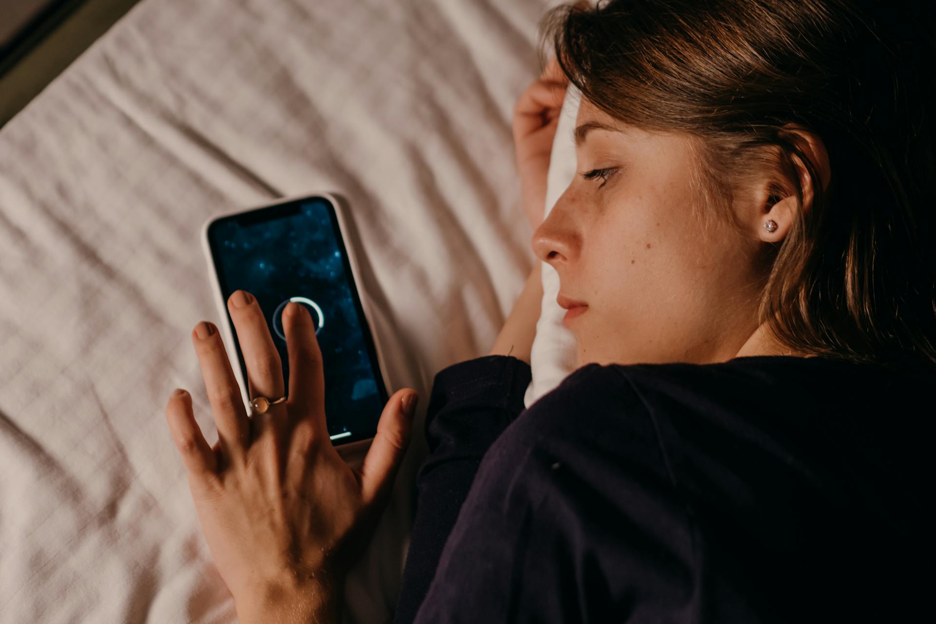 Mujer tumbada en una cama mientras usa su smartphone | Fuente: Pexels