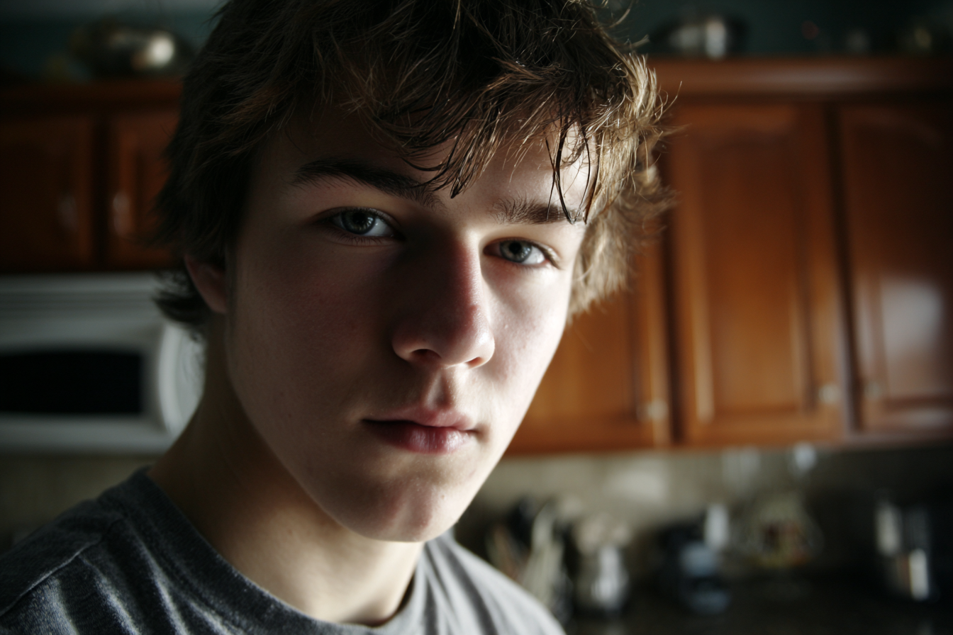 Un adolescente de pie en la cocina y mirando a alguien | Fuente: Midjourney