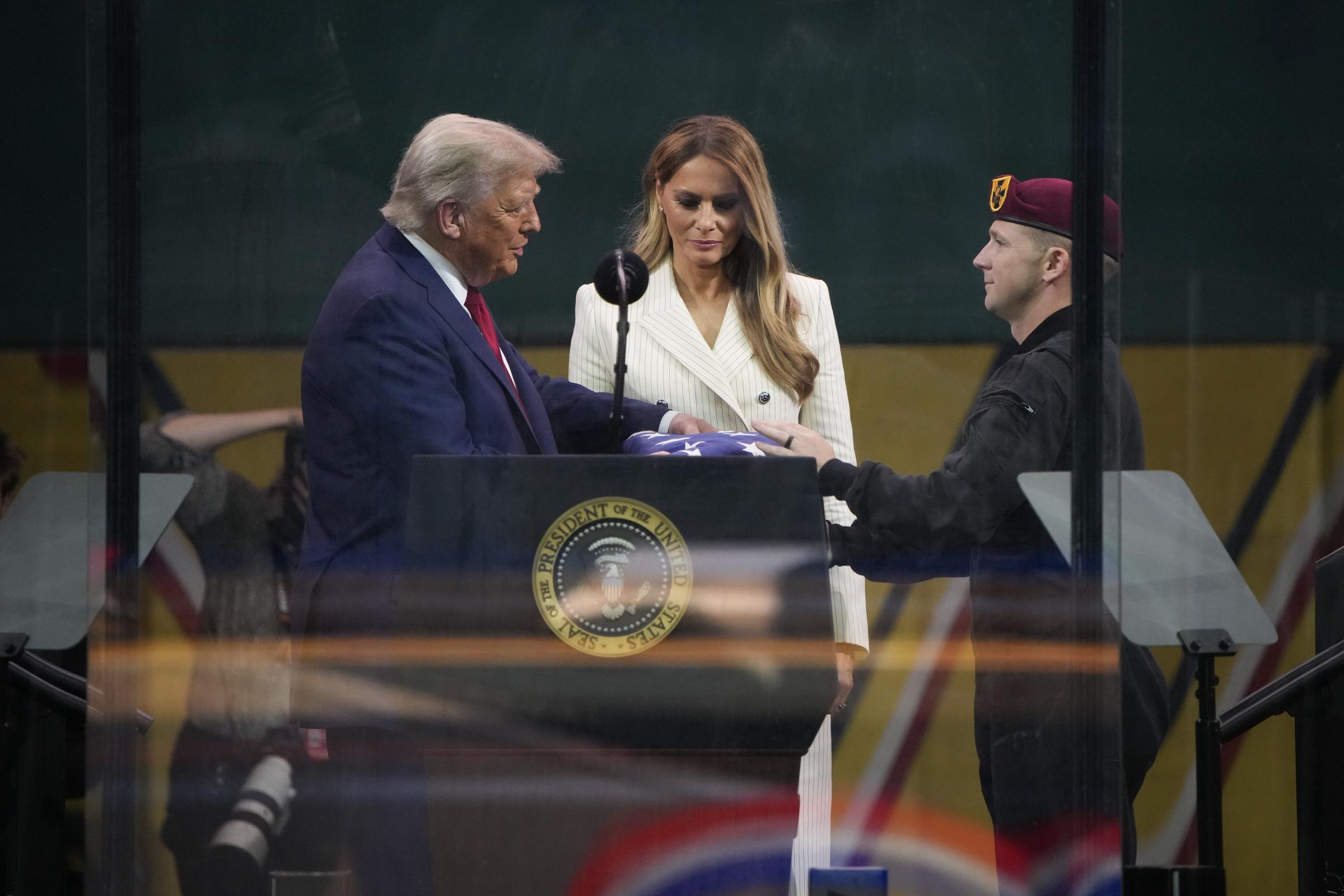 Donald y Melania Trump permanecen juntos mientras él recibe una bandera estadounidense de manos de un miembro del equipo de paracaidistas del Ejército de EEUU al final del desfile del Ejército de EEUU en Washington, DC, el 14 de junio de 2025 | Fuente: Getty Images