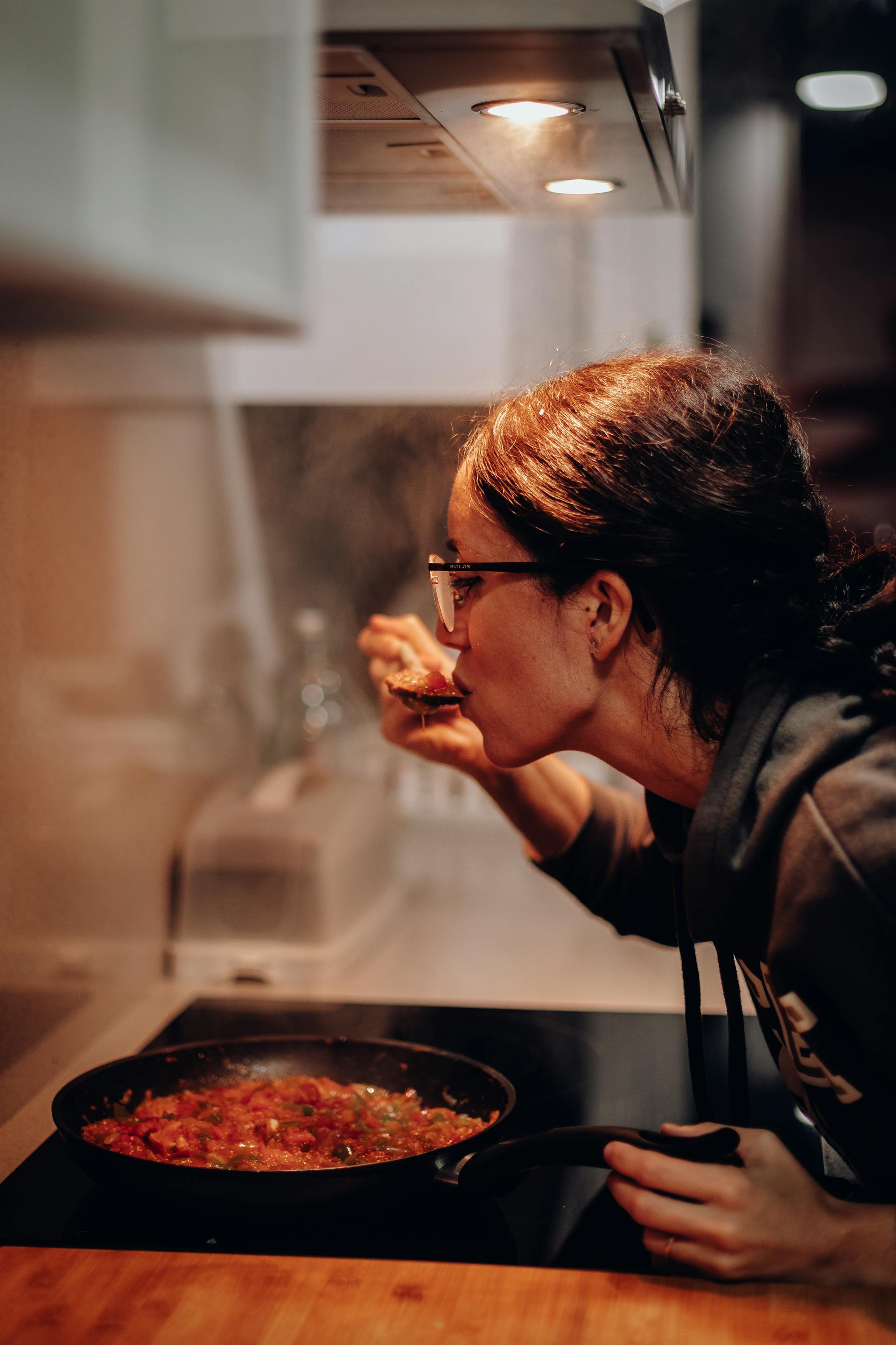 Una mujer probando comida de una sartén | Fuente: Pexels