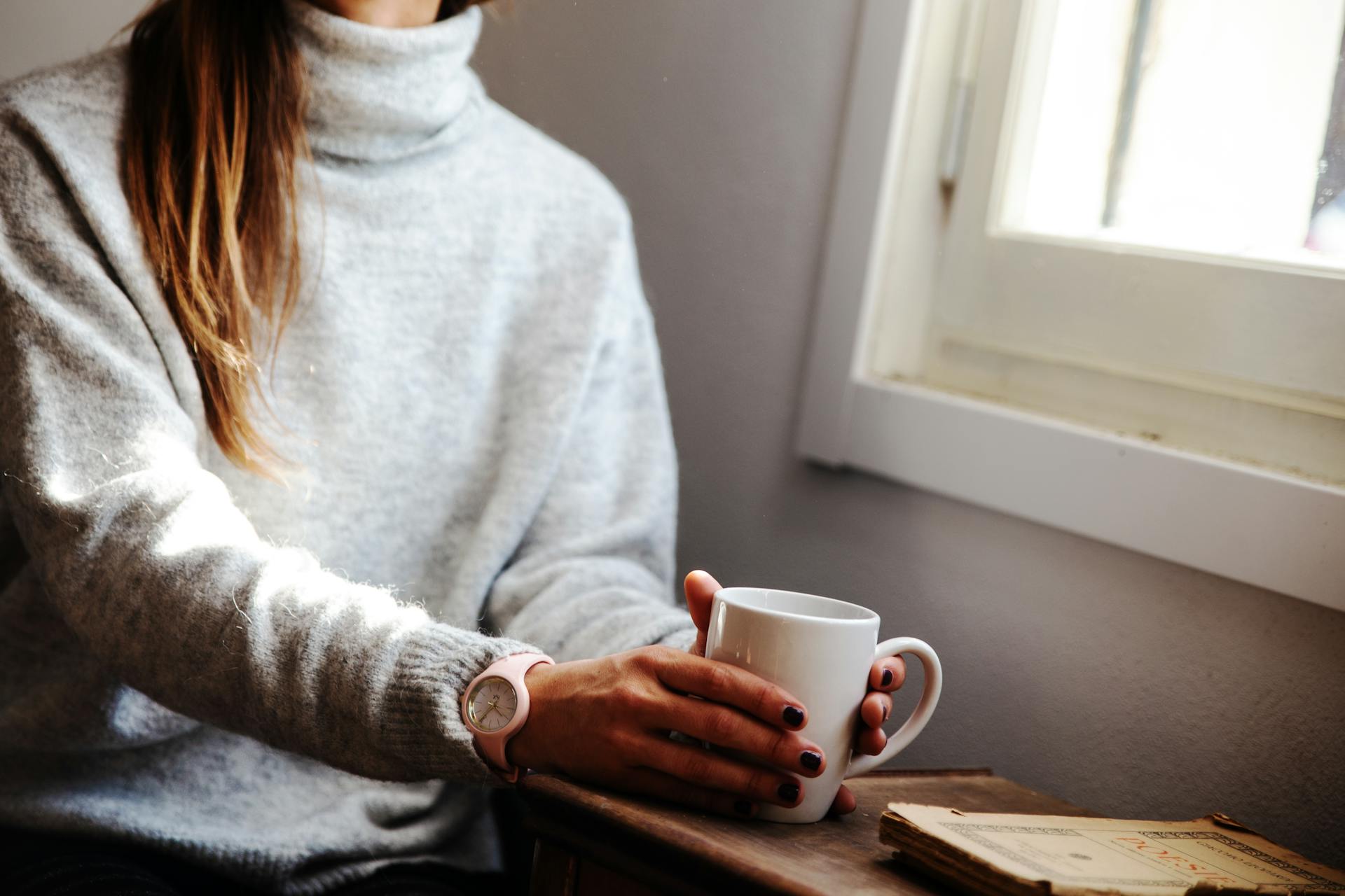 Una mujer sostiene una taza de café sentada junto a una ventana | Fuente: Pexels