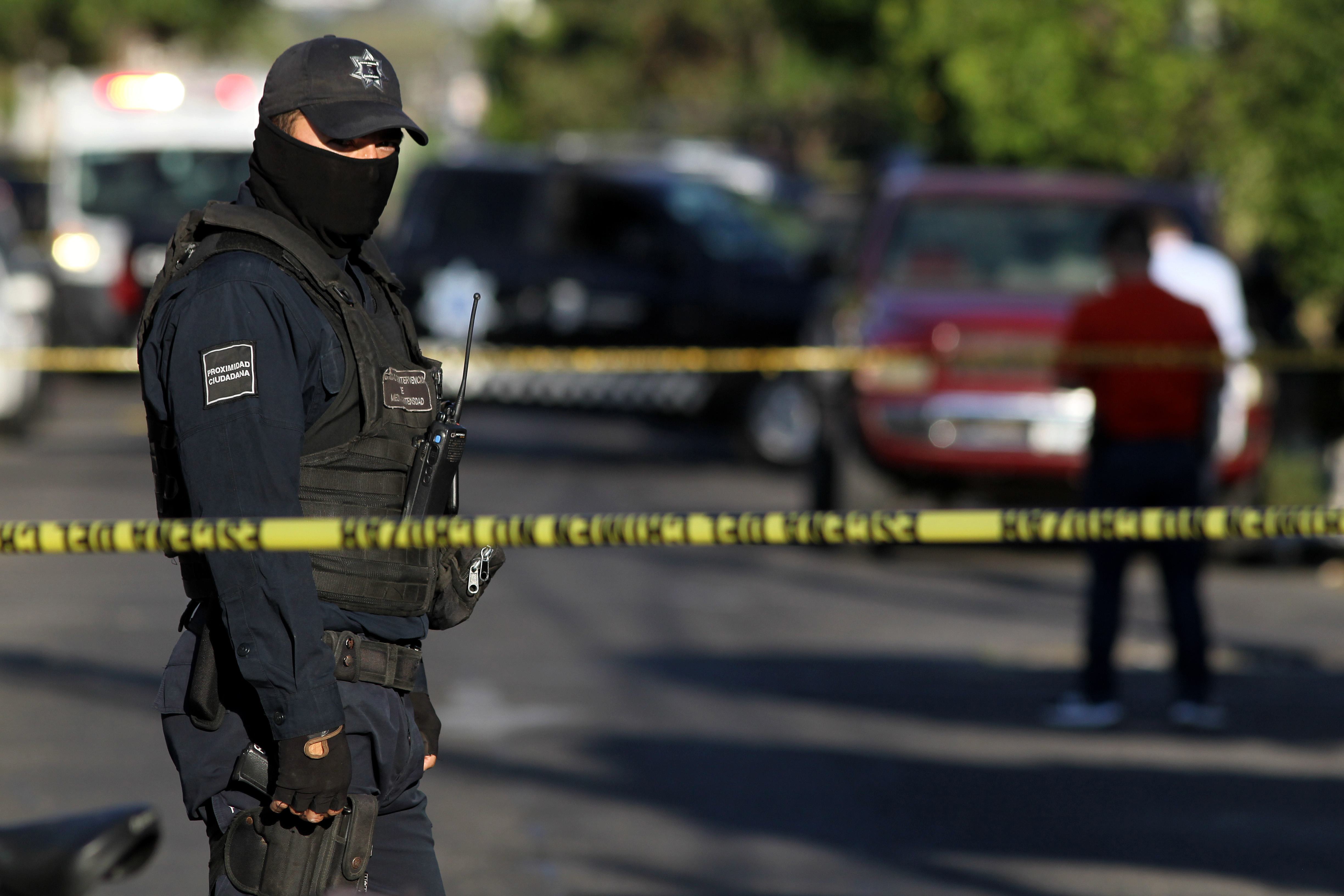 Un oficial de policía hace guardia mientras los fiscales estatales inspeccionan una camioneta encontrada abandonada con los cuerpos de seis hombres, algunos de ellos decapitados, que se cree fueron asesinados por presuntos traficantes de un cártel rival, en el barrio de Morelos en Guadalajara, México, el 6 de marzo de 2018. | Fuente: Getty Images.
