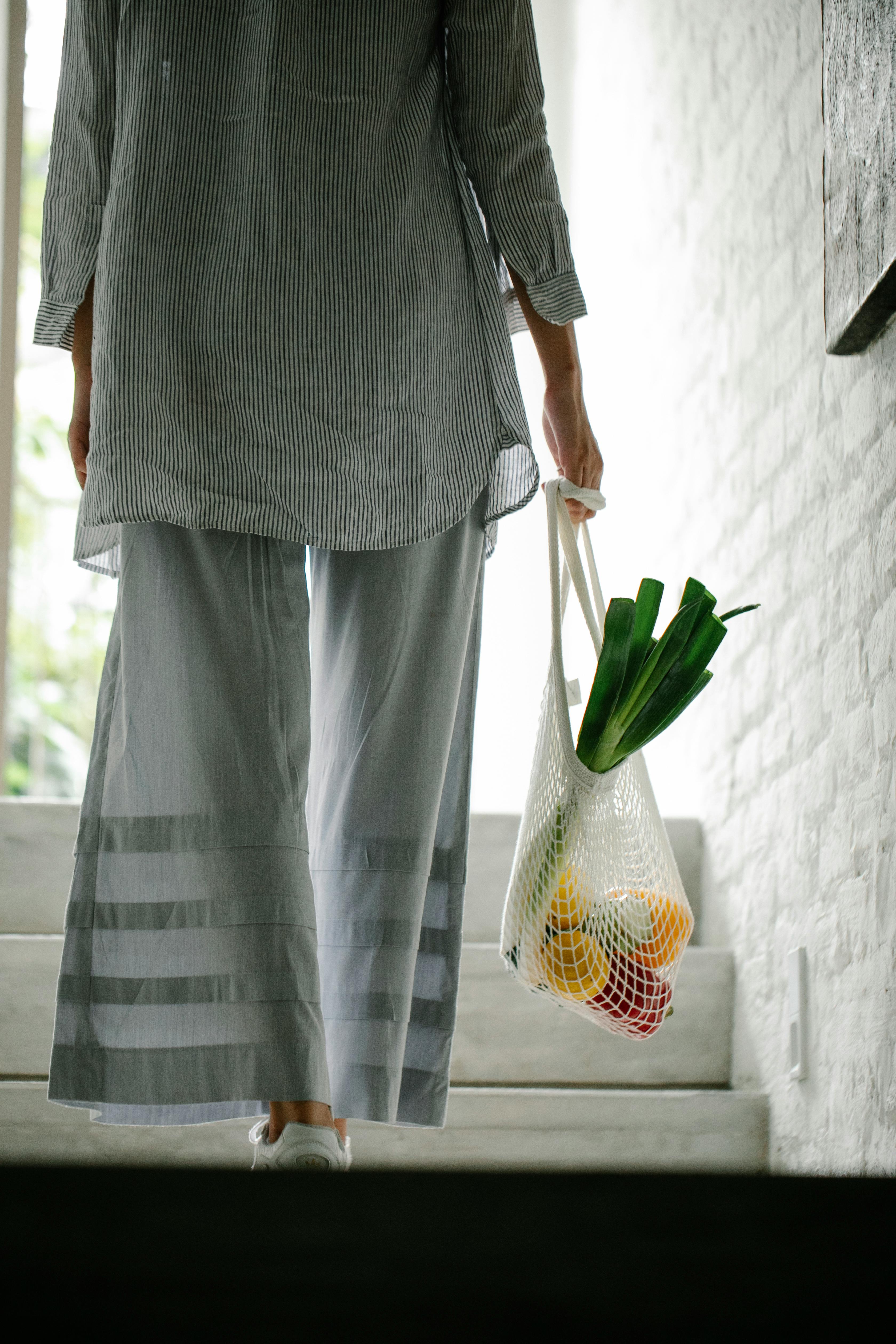 Una mujer lleva verduras en una bolsa por la escalera de una casa | Fuente: Pexels