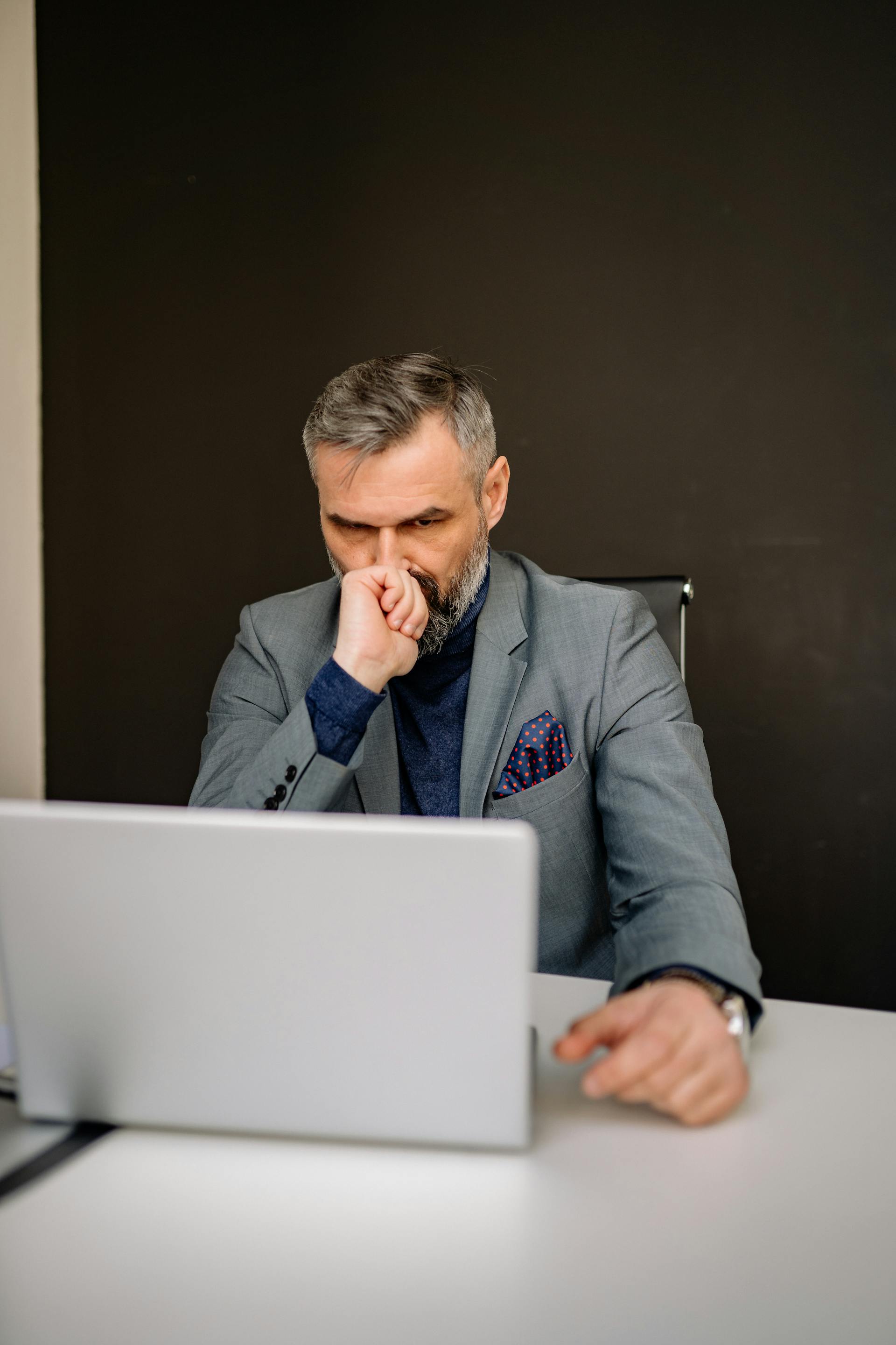 Un hombre mirando su portátil sentado en la oficina | Fuente: Pexels