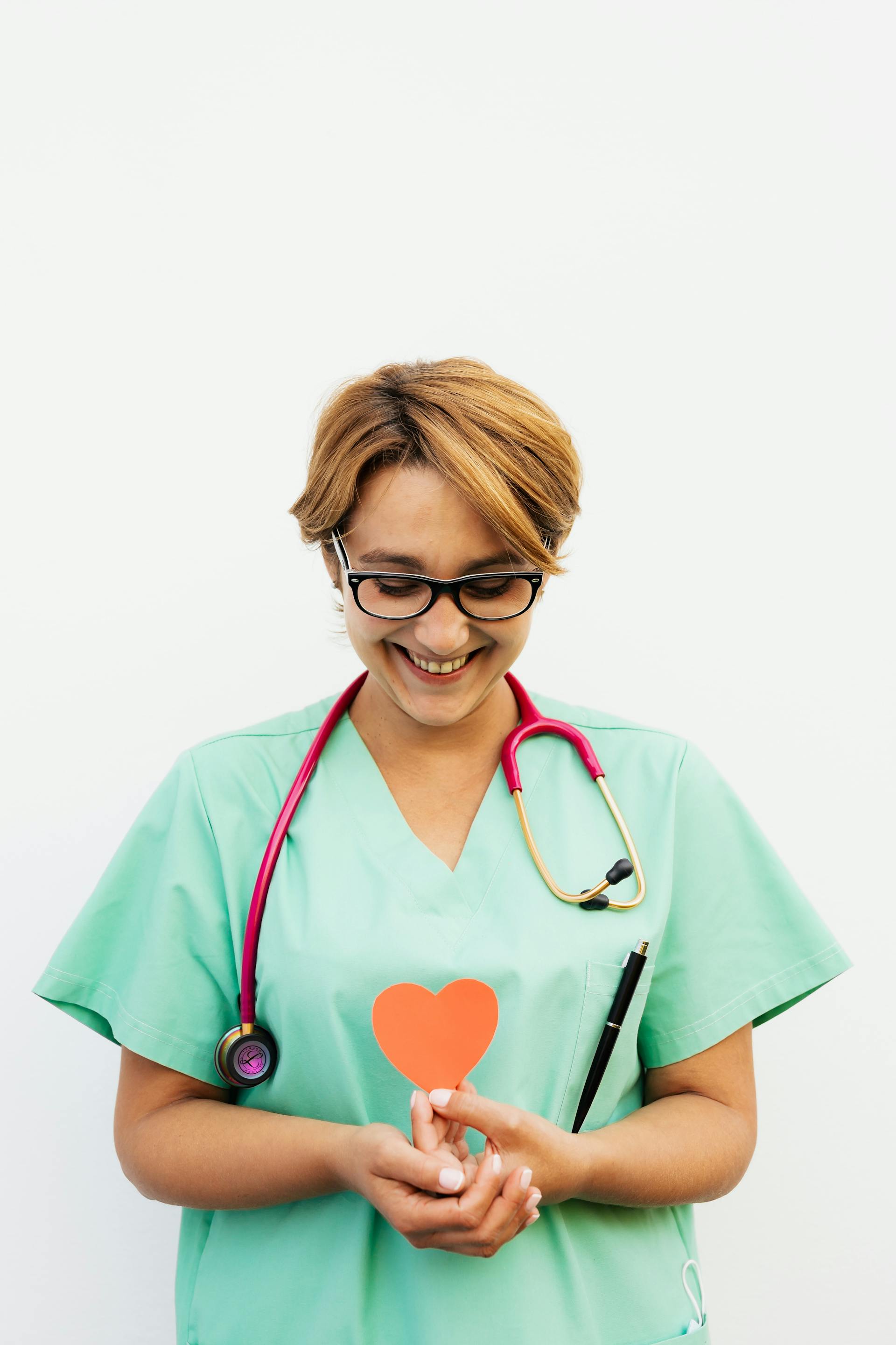 Una enfermera sonriente sosteniendo un corazón de papel rojo | Fuente: Pexels