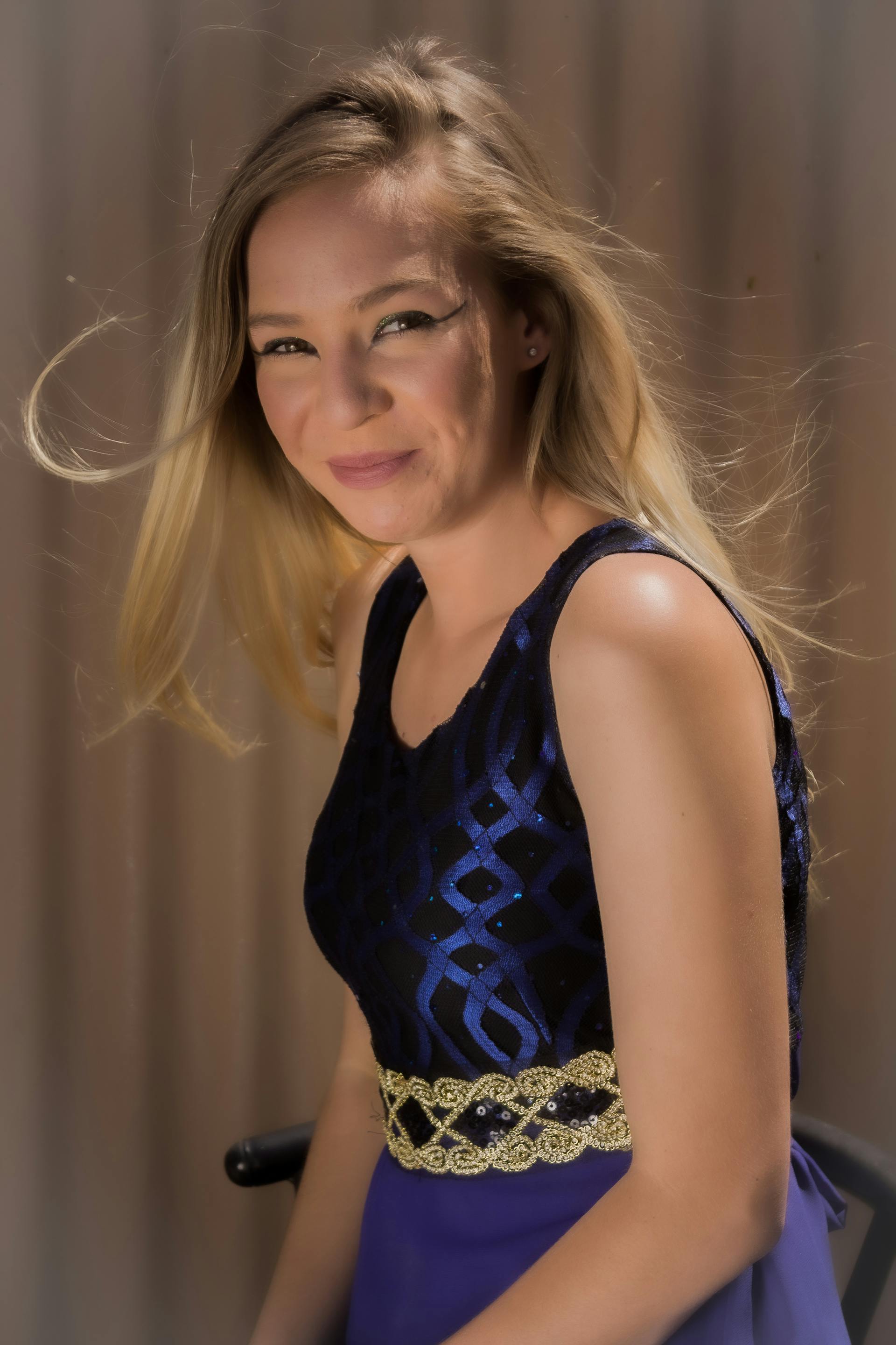 Una bella joven de pelo rubio sonríe mientras lleva un vestido azul y dorado brillante | Fuente: Pexels
