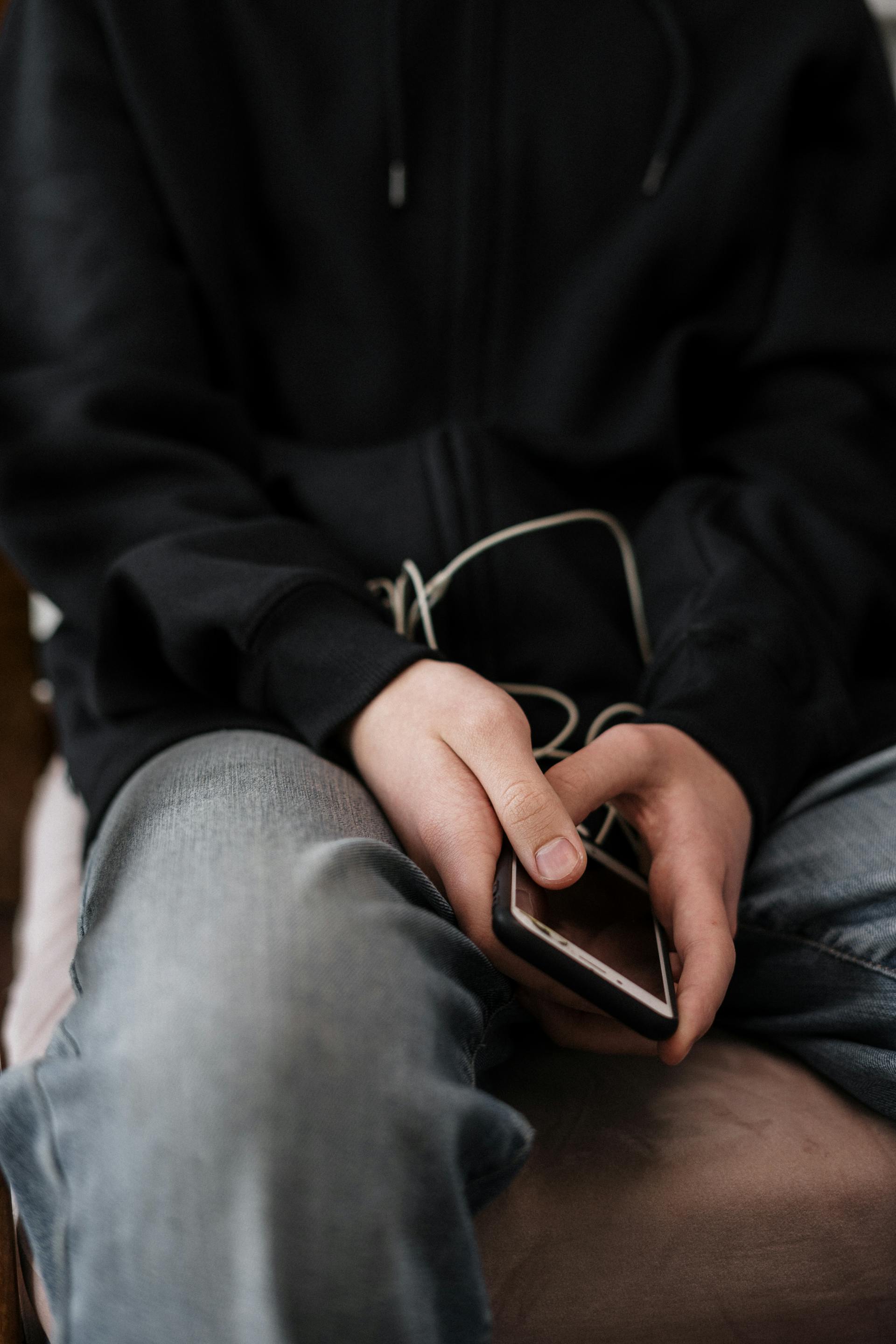 Primer plano de una persona con chaqueta y jeans que sostiene un teléfono | Fuente: Pexels