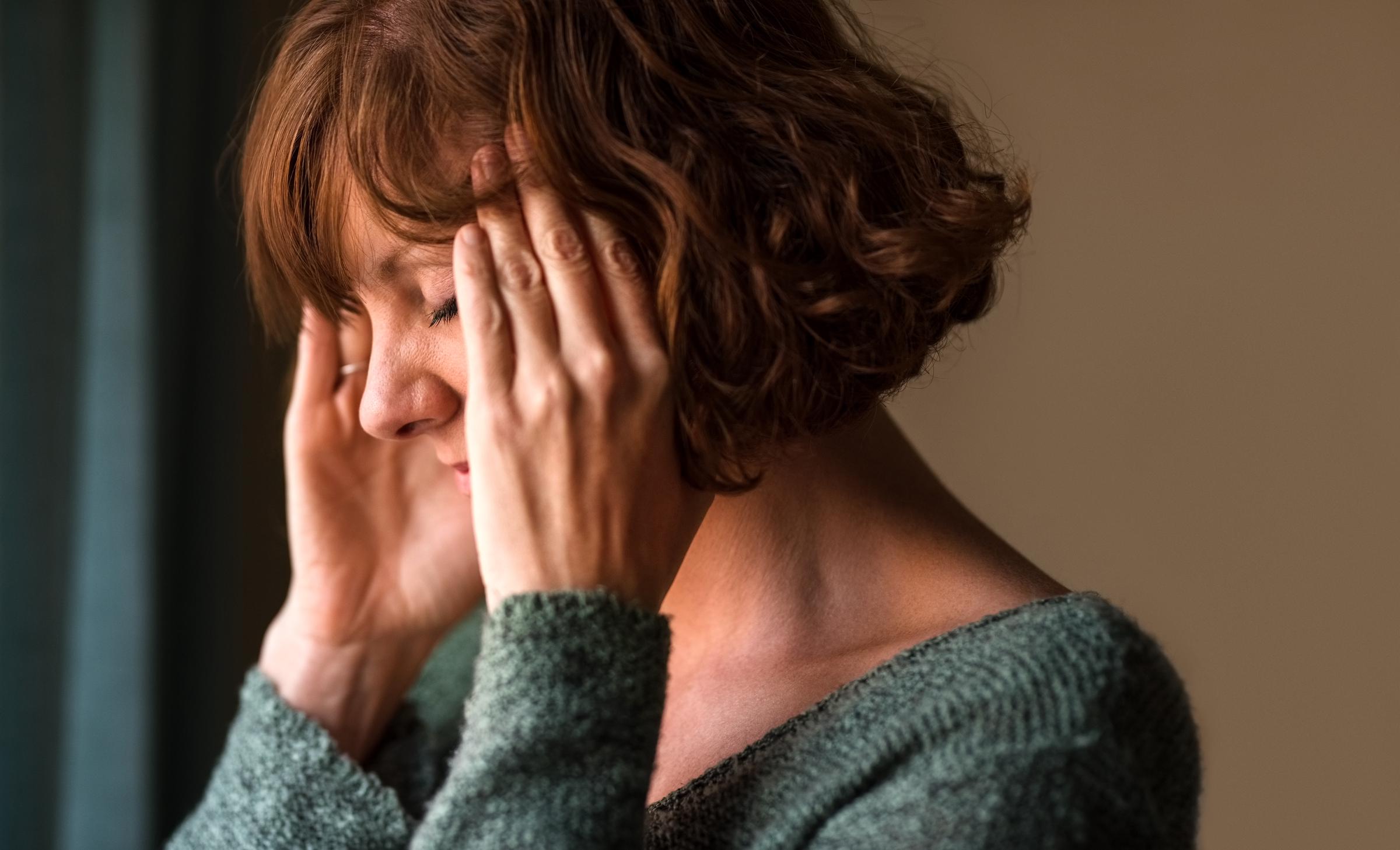 Mujer con dolor de cabeza, frotándose las sienes con molestia | Fuente: Getty Images