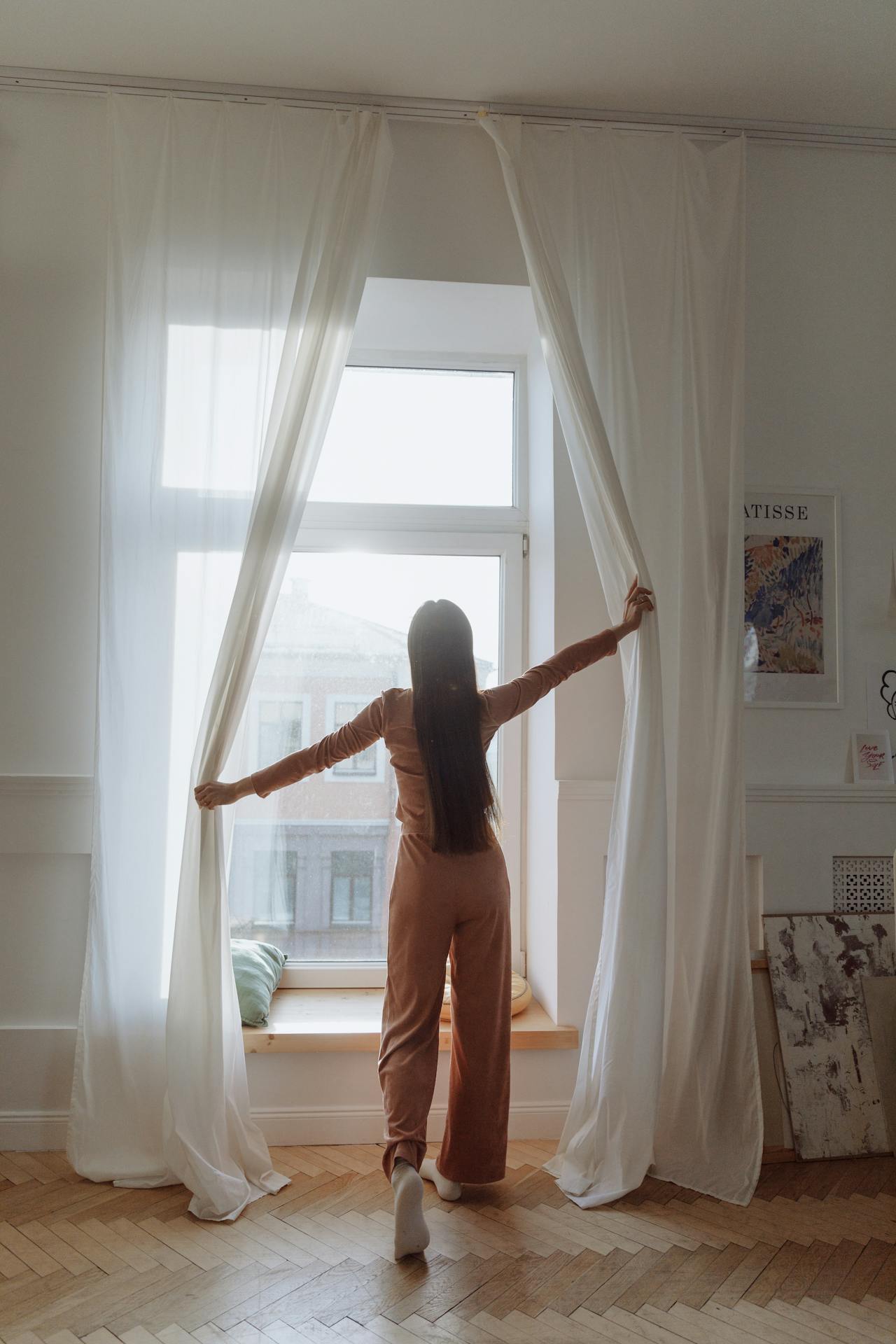 Una mujer de pie cerca de la ventana y abriendo las cortinas | Fuente: Pexels